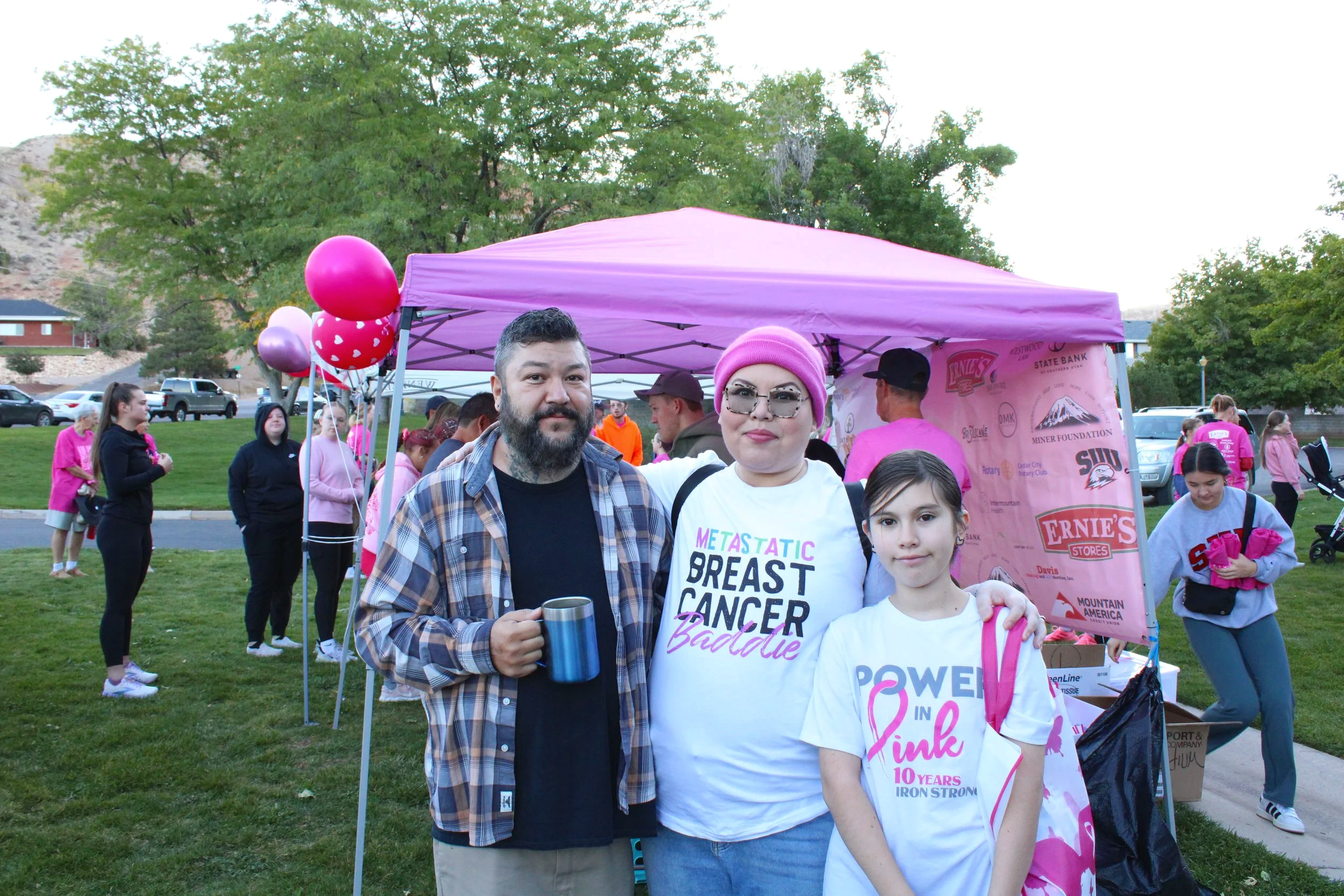 Group of people participating in a breast cancer awareness event outdoors, with some wearing pink clothing and a tent in the background.