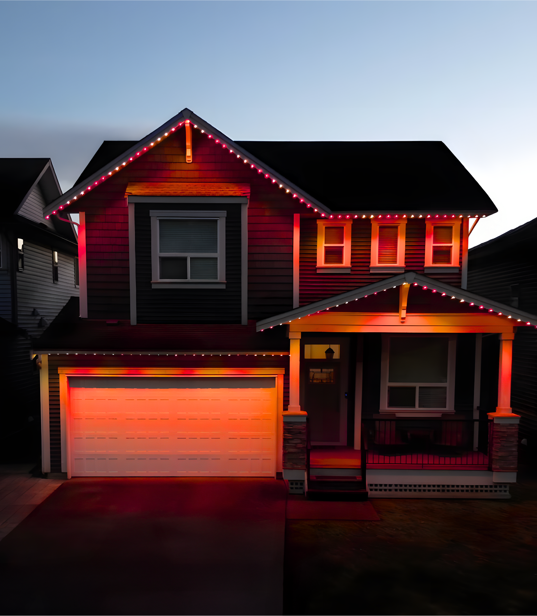 A two-story house decorated with red and white Christmas lights along the roofline and around the garage door, taken during dusk or early evening.