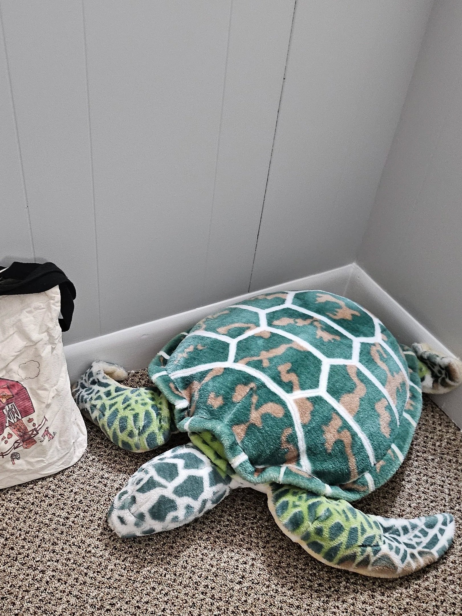 A pile of towels with green, white, and tan geometric patterns on a carpeted floor, with a gray wall in the background.