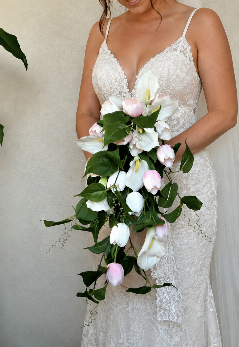 A bride in a white lace wedding dress holding a cascading bouquet of white and pink tulips, roses, and greenery in the Tri-Cities, Washington
