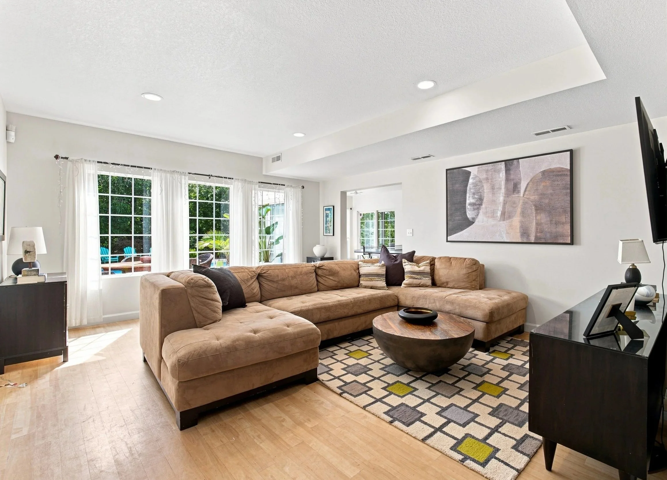 Living room with large sectional sofa, abstract wall art, coffee table, and windows with white curtains