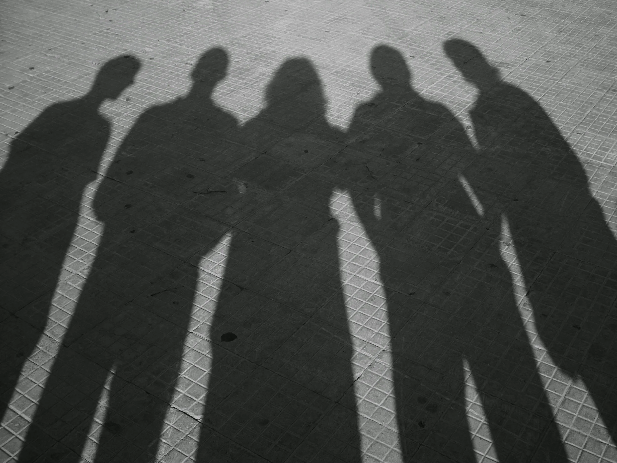 Shadows of five people on a tiled ground, with some cracks and small marks on the tiles.