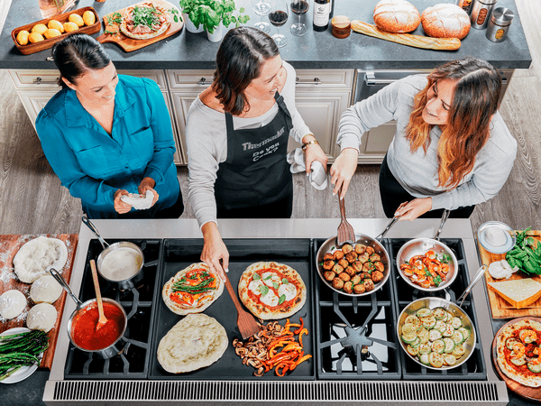 three women cooking together on a modern kitchen stove