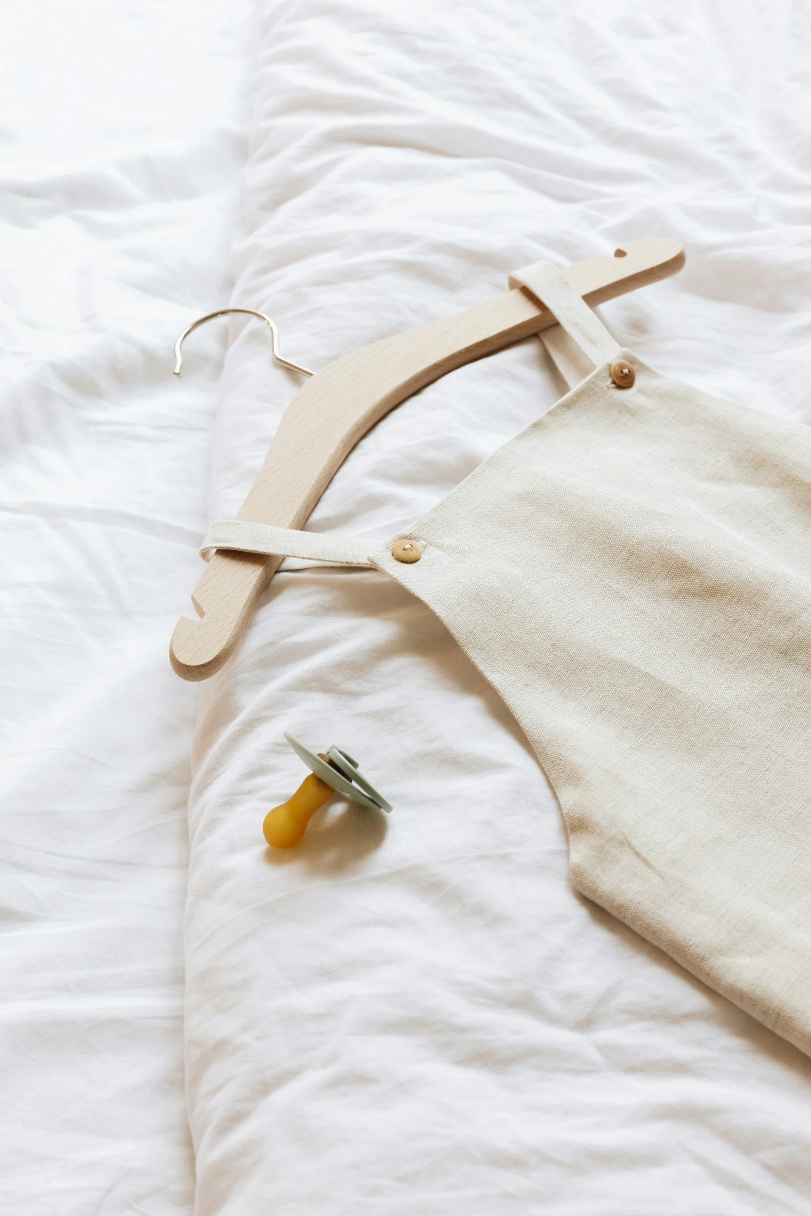 A white bed with a wooden hanger, a cream-colored fabric bag with buttons, a yellow and gray gently curved toy on the bed.