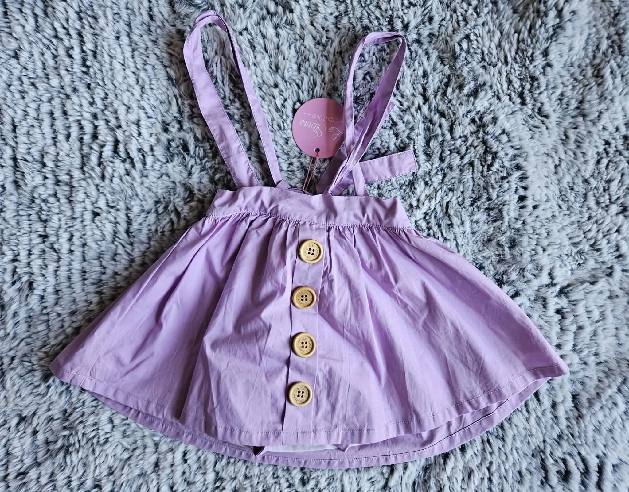 A pink dress with buttons laid on a fluffy black and white rug.
