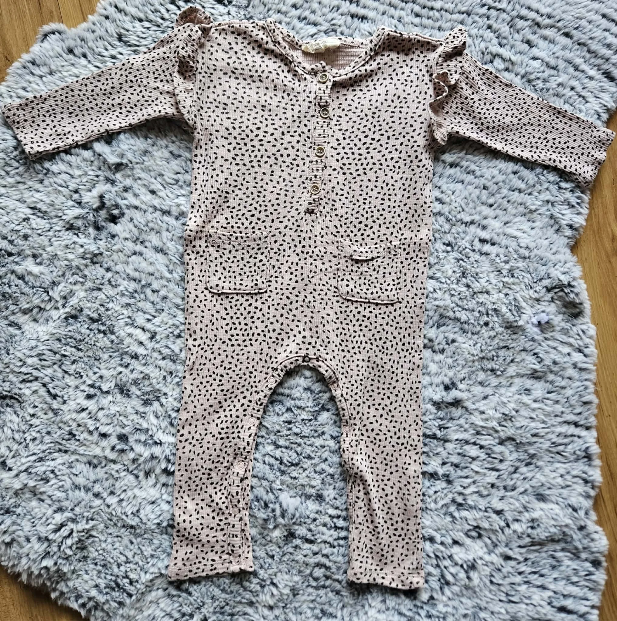 A pink baby onesie with black polka dots spread out on a gray and white fluffy rug.