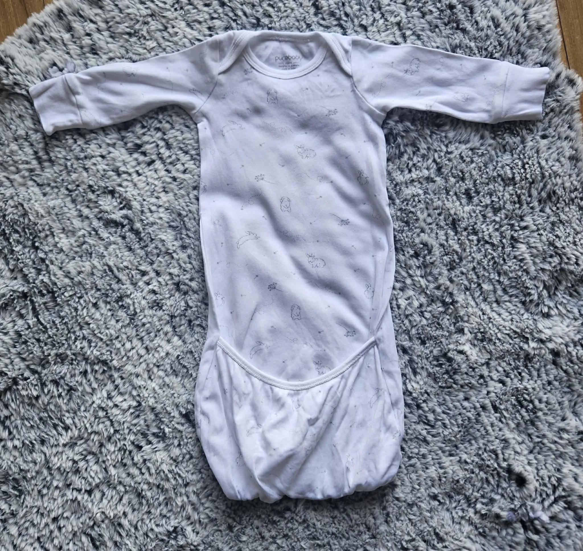 A white baby onesie with animal print designs laid out on a textured rug.