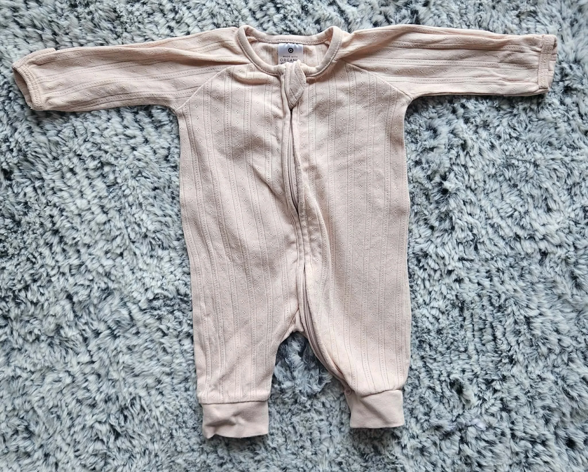 A pink baby onesie with a zipper in the middle, laid flat on a fluffy gray and white textured rug.