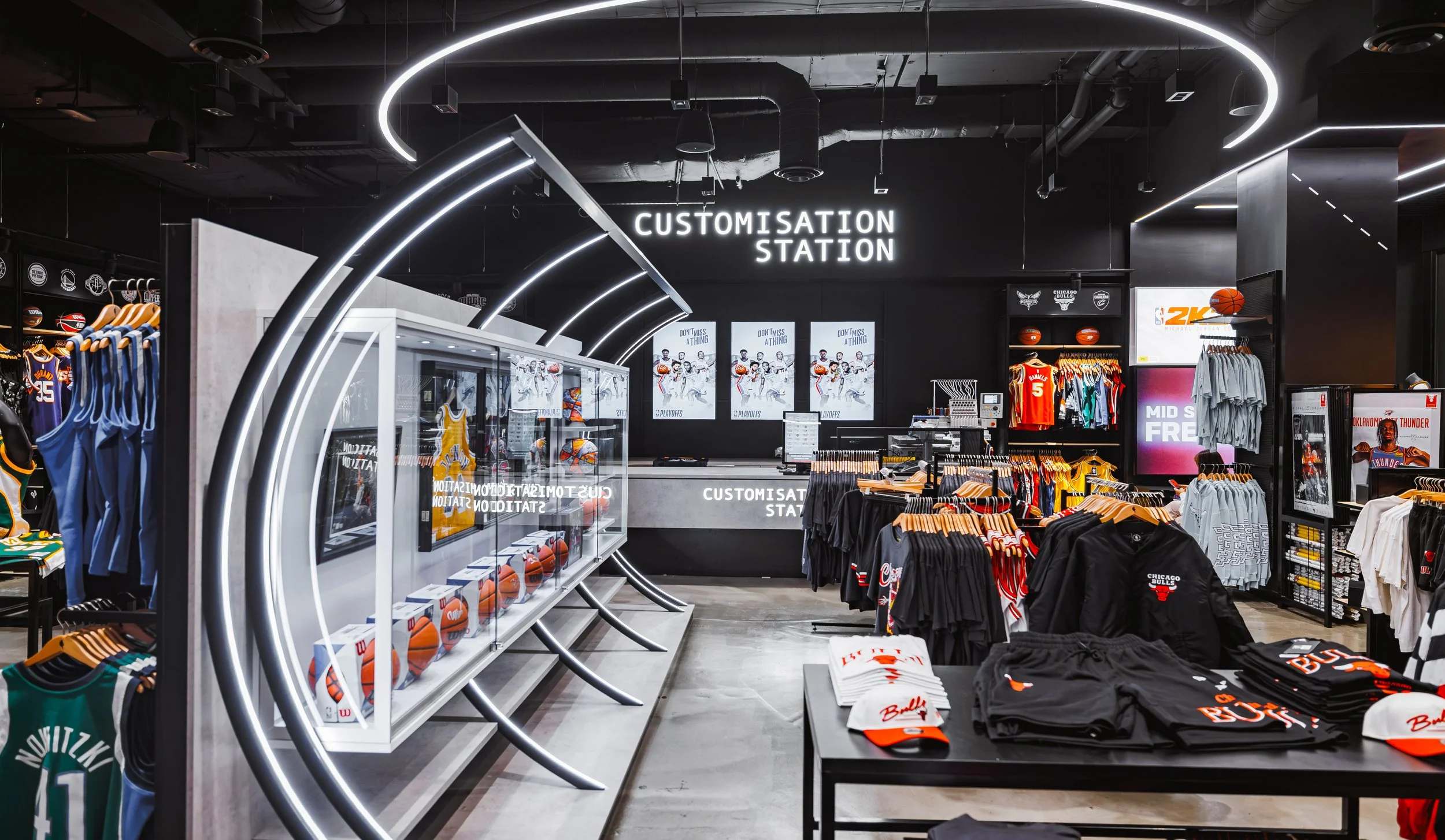 A retail store with sports apparel and merchandise, including basketball jerseys, caps, and clothing, organized on racks and shelves under modern lighting.