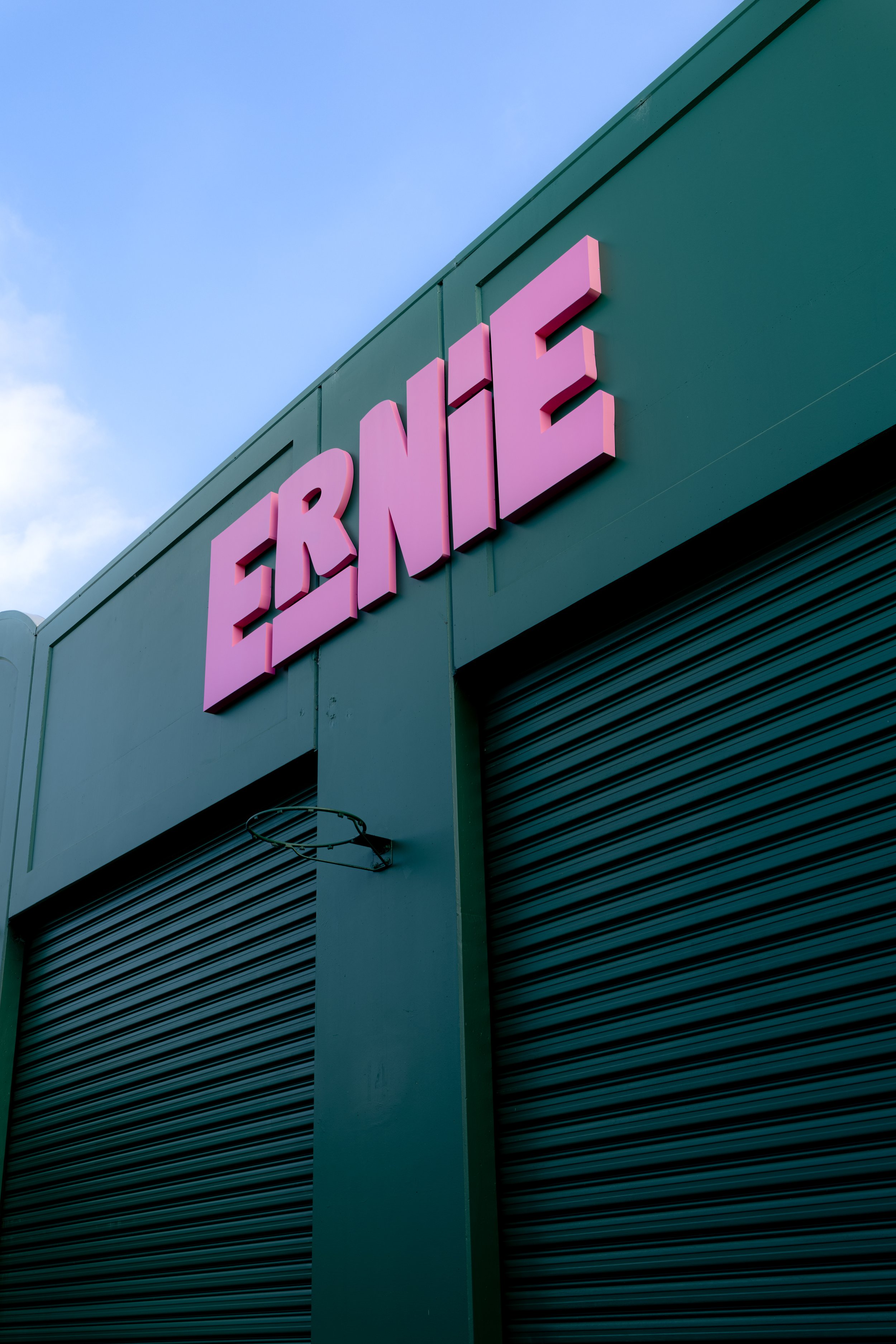 Close-up of a building's exterior with a pink sign spelling 'ERINE' on a green wall, with a cloudy sky in the background.