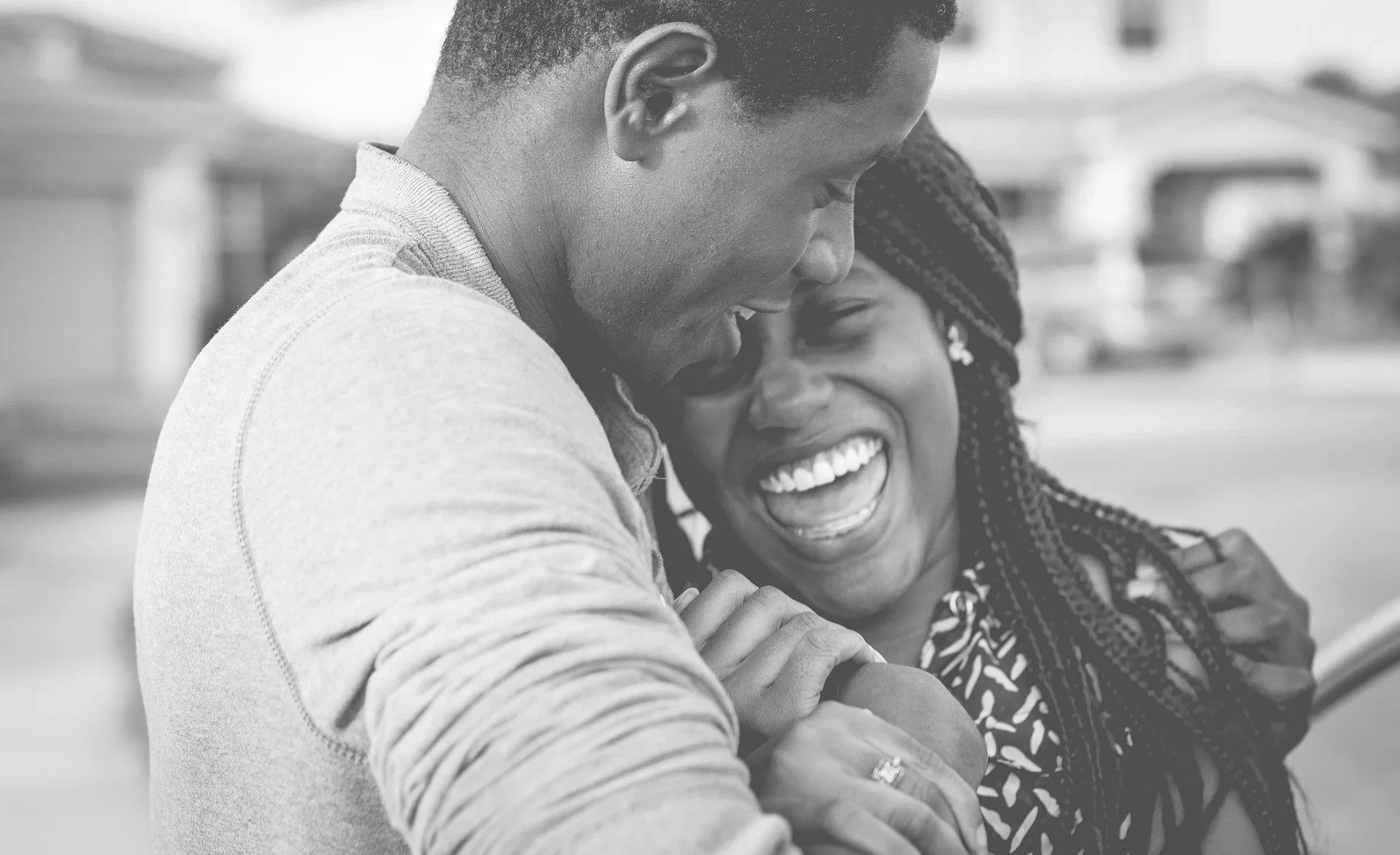 A black and white photo of a couple hugging and laughing outdoors.