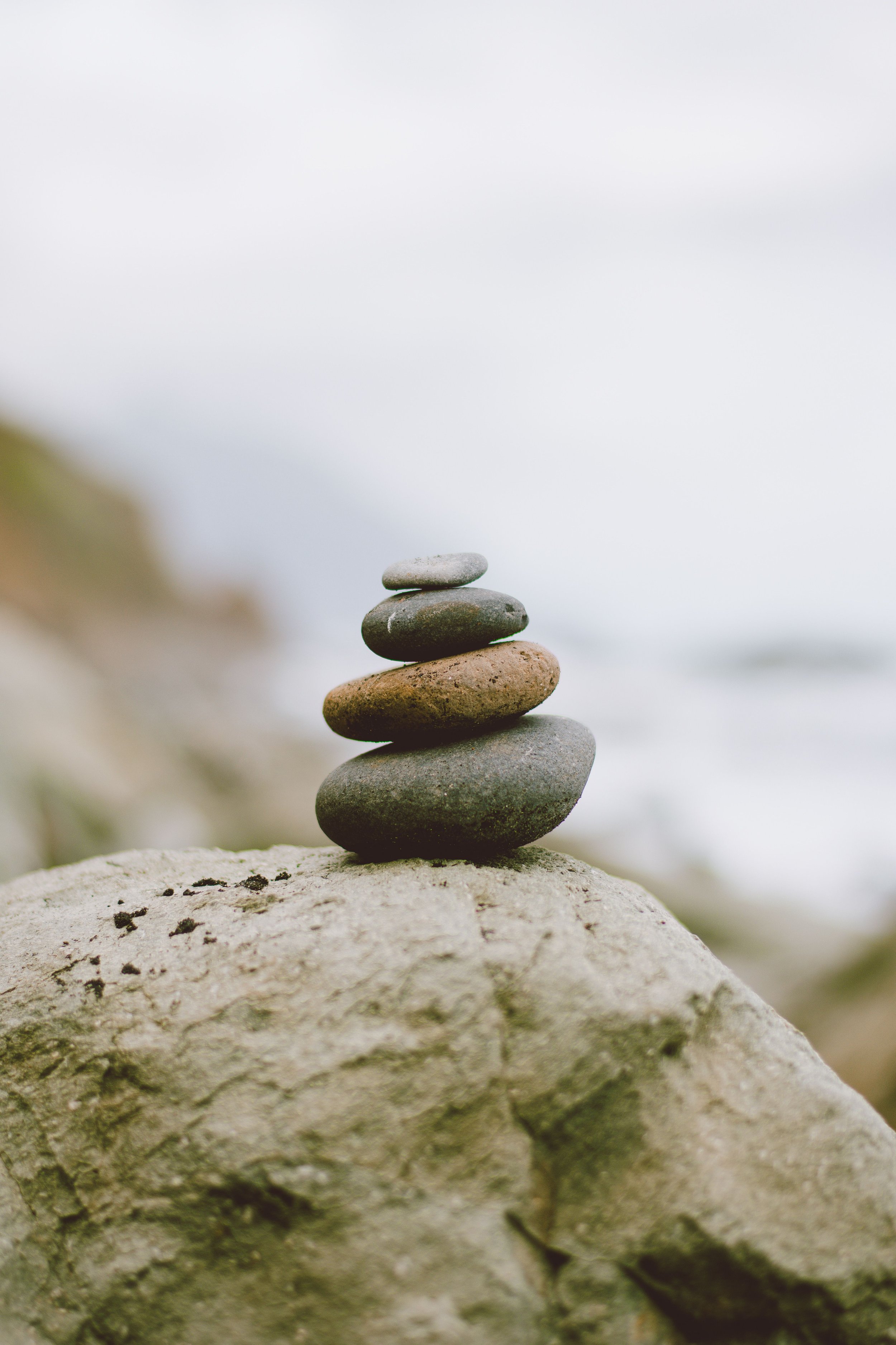 A pile of five balancing stones on a large rock with blurred natural background.