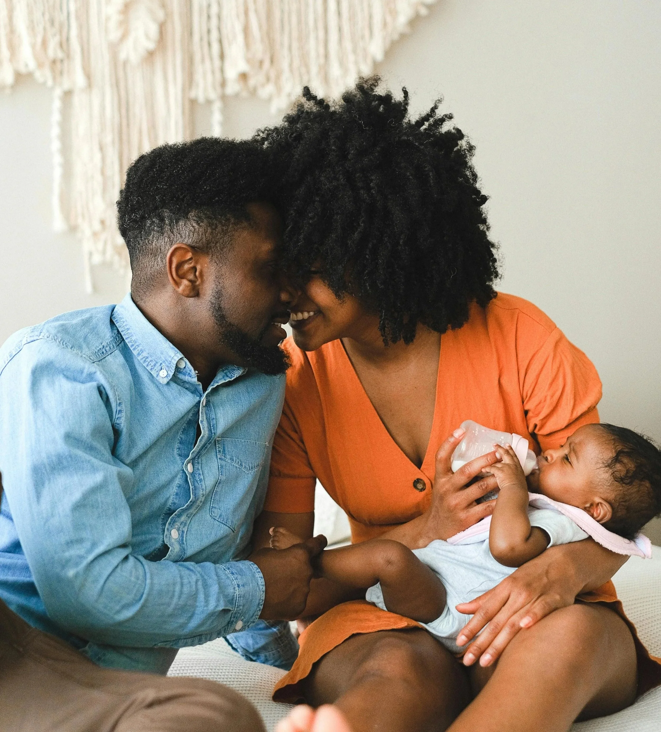 A man and a woman are smiling and leaning their foreheads together while holding a baby, with affectionate and joyful expressions.