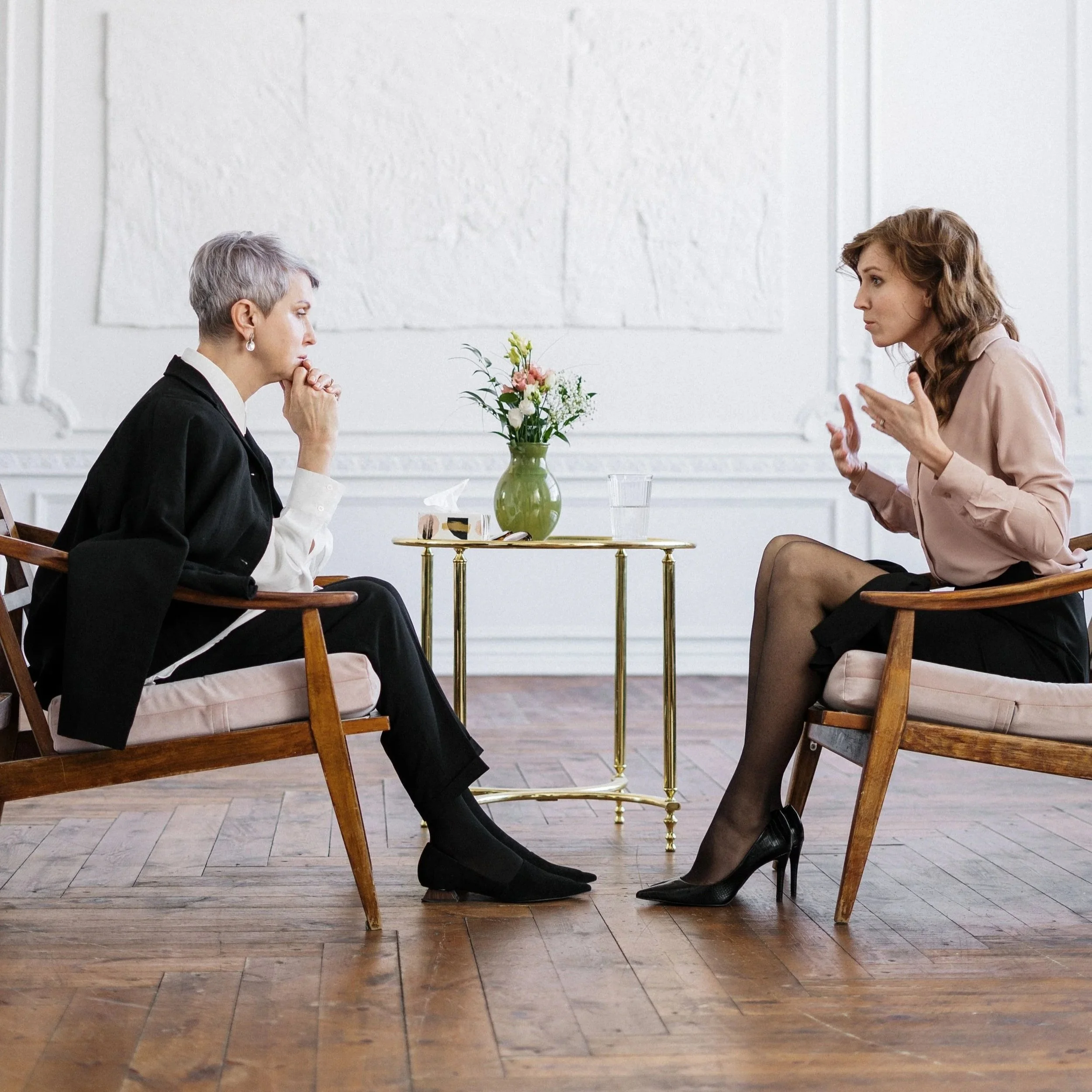 Two women having a serious conversation across a small table with a flower arrangement.
