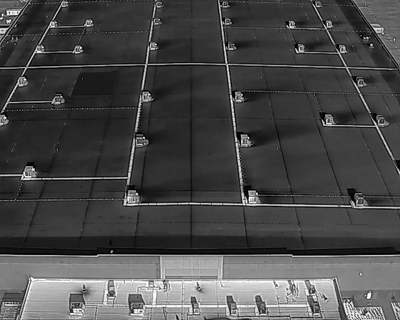 Black and white aerial view of a flat rooftop with multiple ventilation units and pipes arranged in a grid pattern.