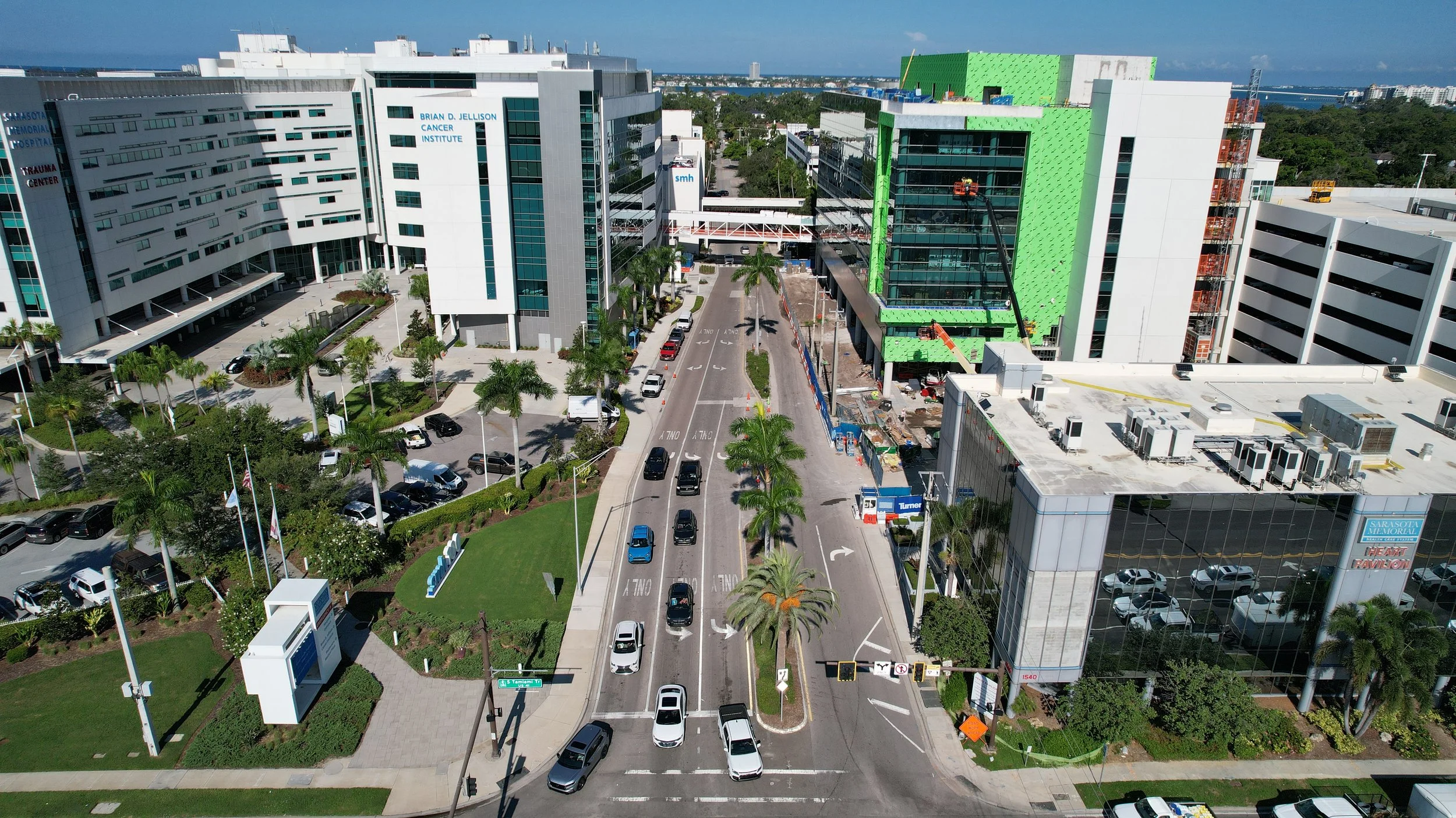 Aerial view of hospital buildings under construction with street traffic and palm trees.