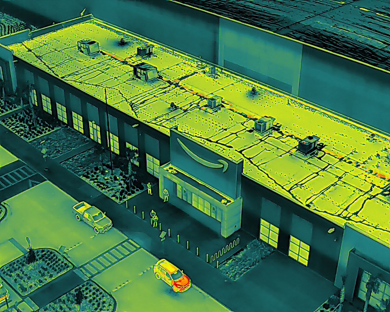 An aerial thermal image of an Amazon fulfillment center showing the roof and parking lot, with people and vehicles visible.