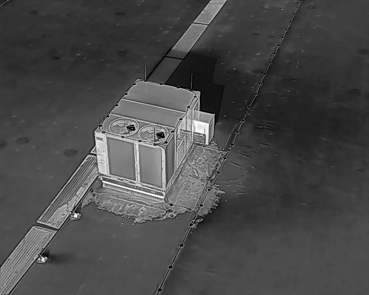 A rooftop HVAC unit with fans on top, adjacent to an access ramp and surrounded by a rooftop safety line.
