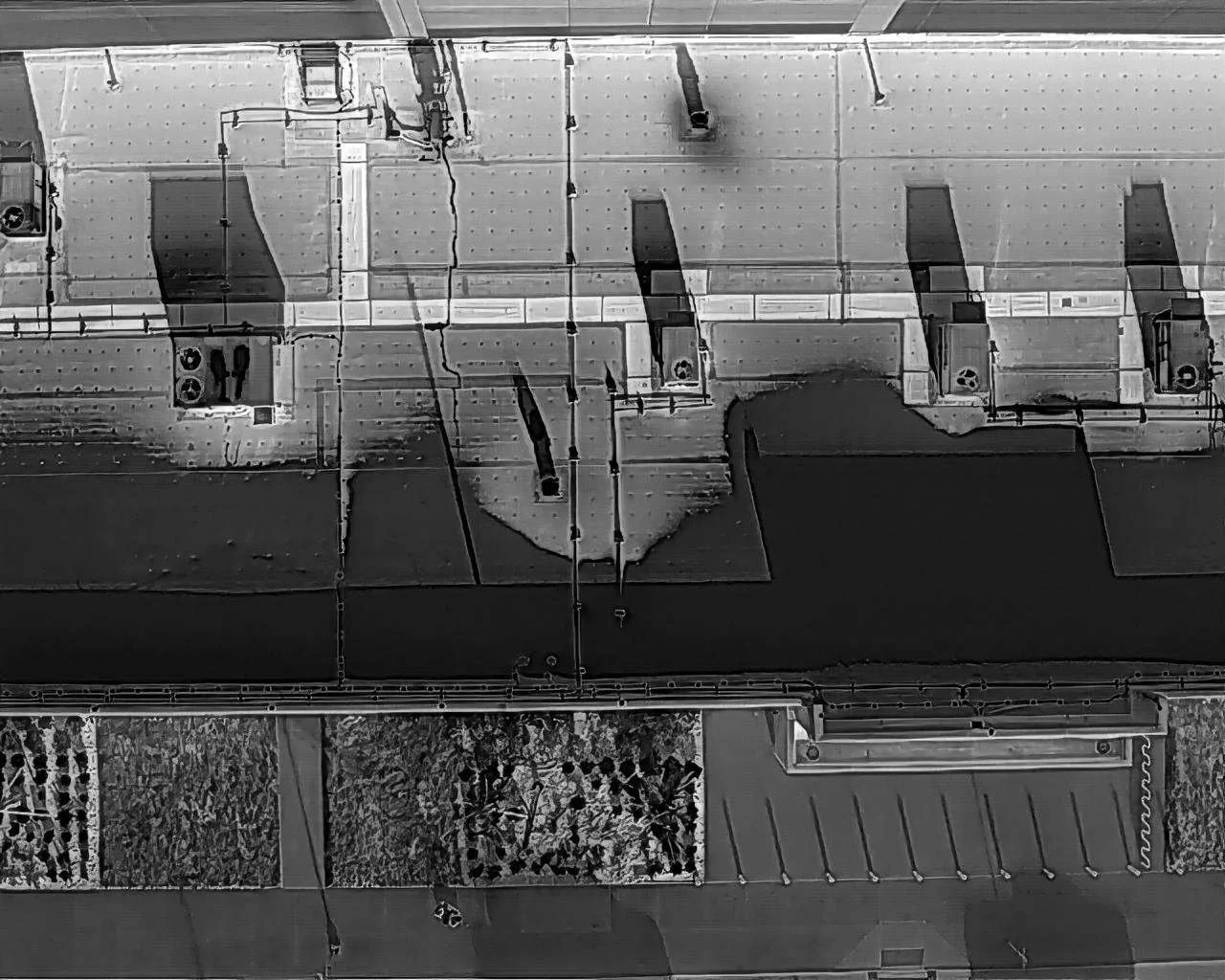 Top-down view of a rooftop showing ventilation units, HVAC equipment, and solar panels in black and white.