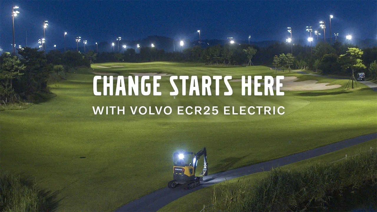 Nighttime golf course with bright lights and a small yellow Volvo ECR25 electric excavator working near the fairway. The text overlay reads "Change Starts Here with Volvo ECR25 Electric."