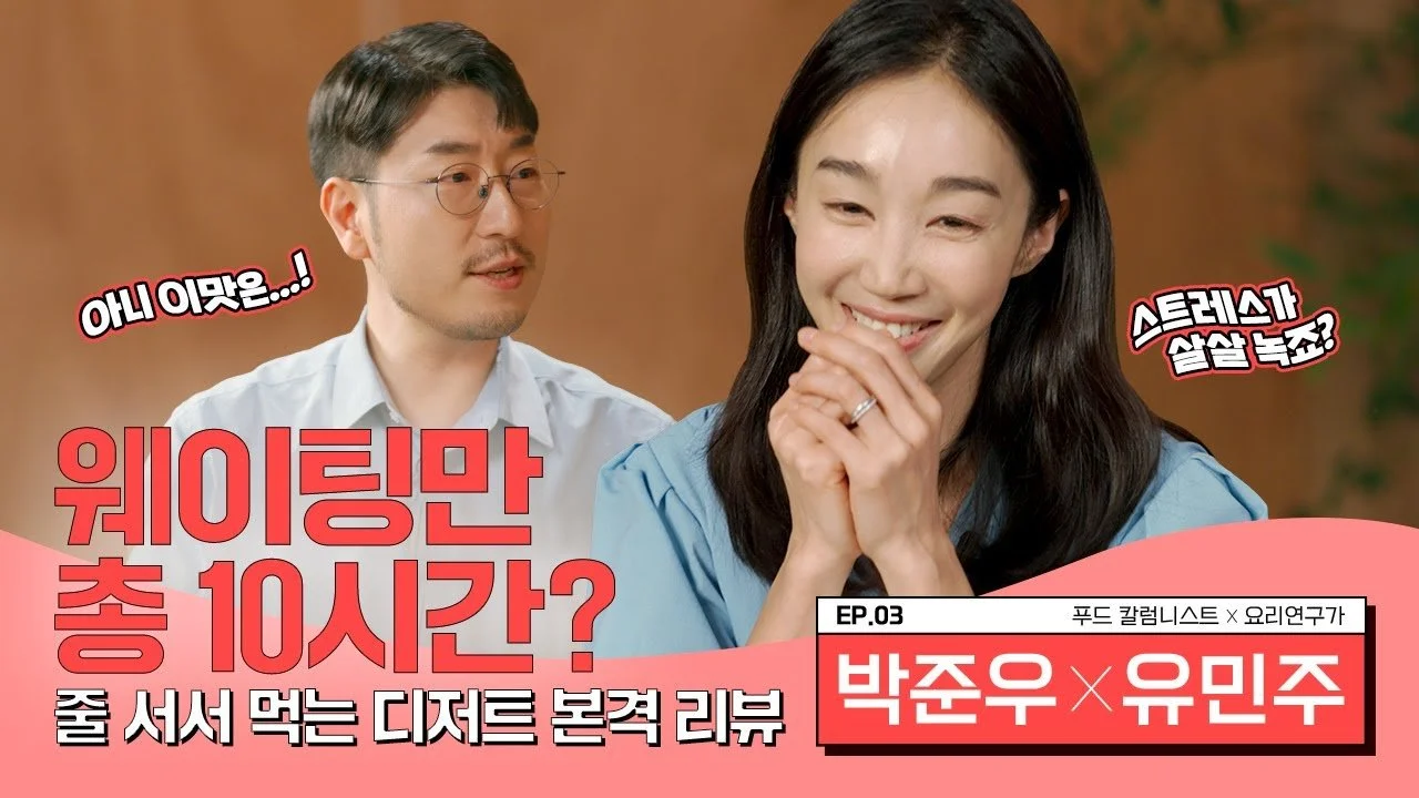 A man and woman engaging in a conversation, with Korean text overlay. The woman is smiling with her hand near her face, and the man is looking at her, wearing glasses. The background is blurred.