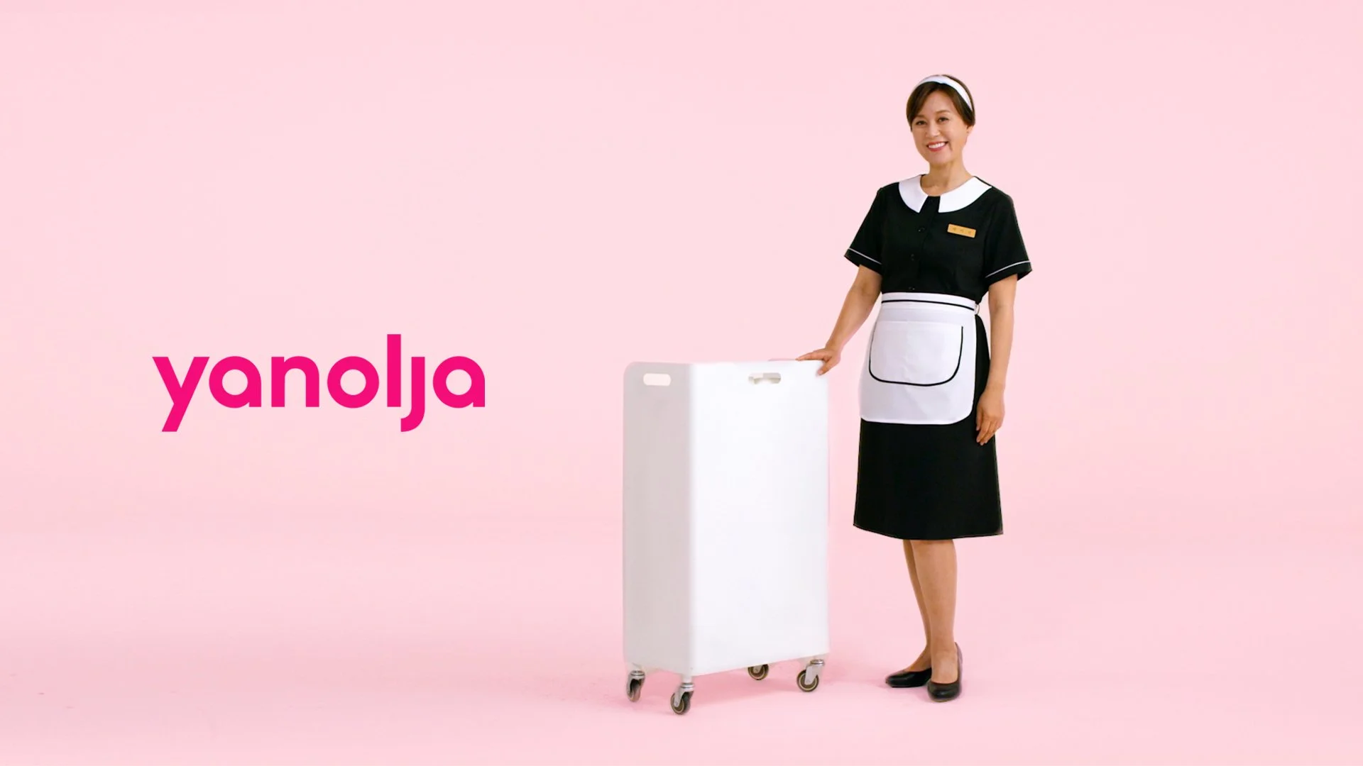A woman dressed as a nurse standing next to a white mobile medical cart, on a pink background, with the word 'yanolja' in pink text.