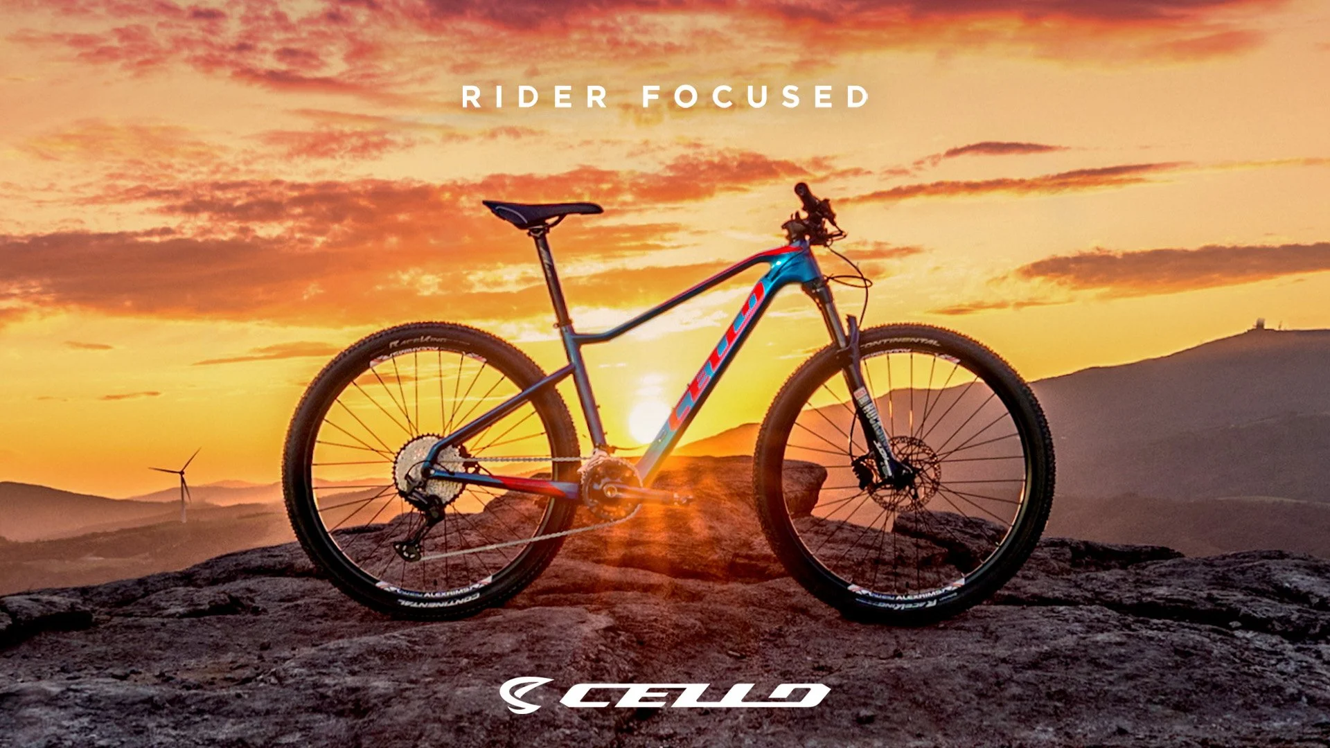 A mountain bike on rocky terrain during sunset with a wind turbine in the background and a mountain range, tagline 'RIDER FOCUSED' at the top, and 'LEVO' logo at the bottom.