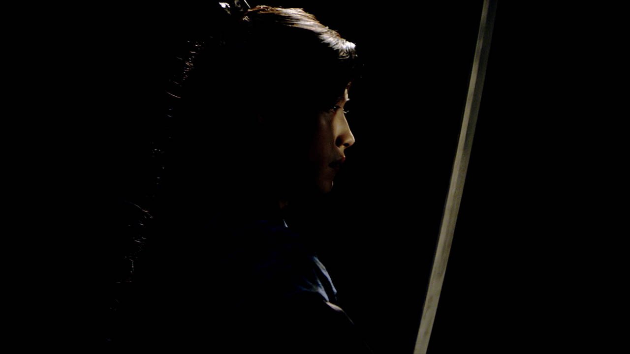 Side profile of a woman in a dark room, illuminated slightly from the side.
