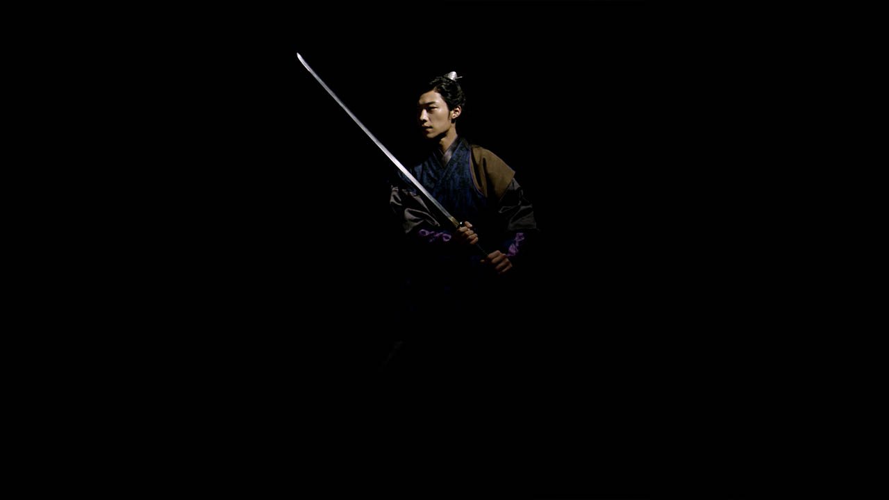 A person dressed in traditional Asian attire holding a sword in a dark setting.