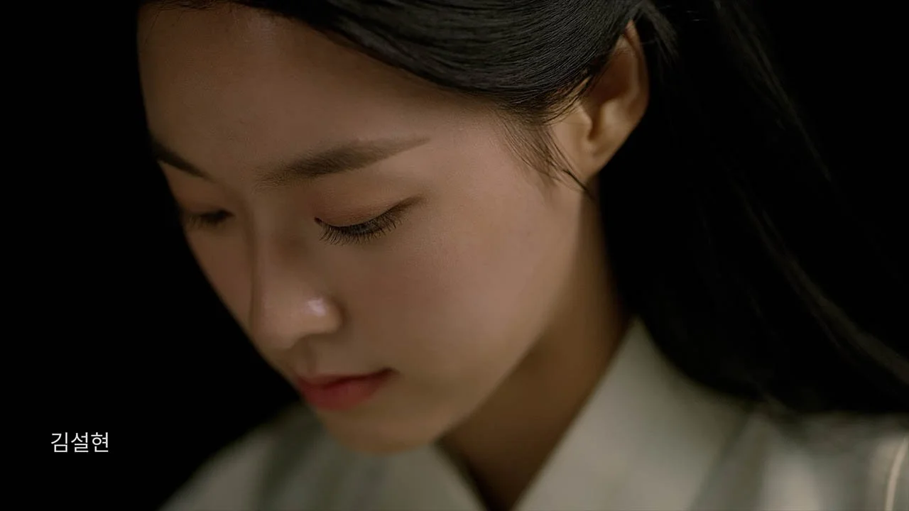 Close-up of a young woman with long dark hair, gentle expression, eyes closed, wearing a light-colored traditional Korean hanbok.