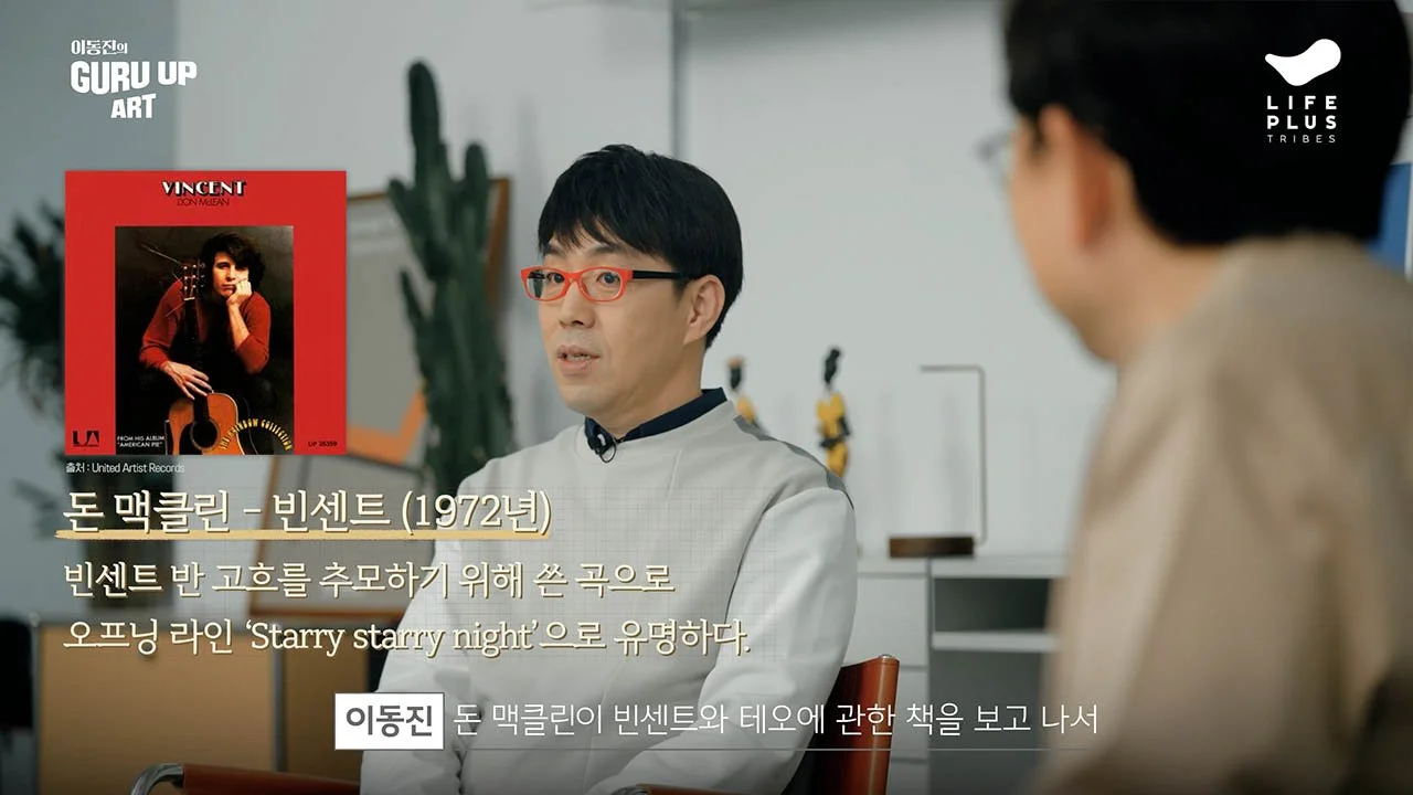 A man with glasses and black hair, wearing a gray jacket, is sitting and speaking to another person in a room with a white wall and plants. There is a picture of Vincent Don McLean with a guitar and a red background, along with Korean text describing his song 'Starry Starry Night.'