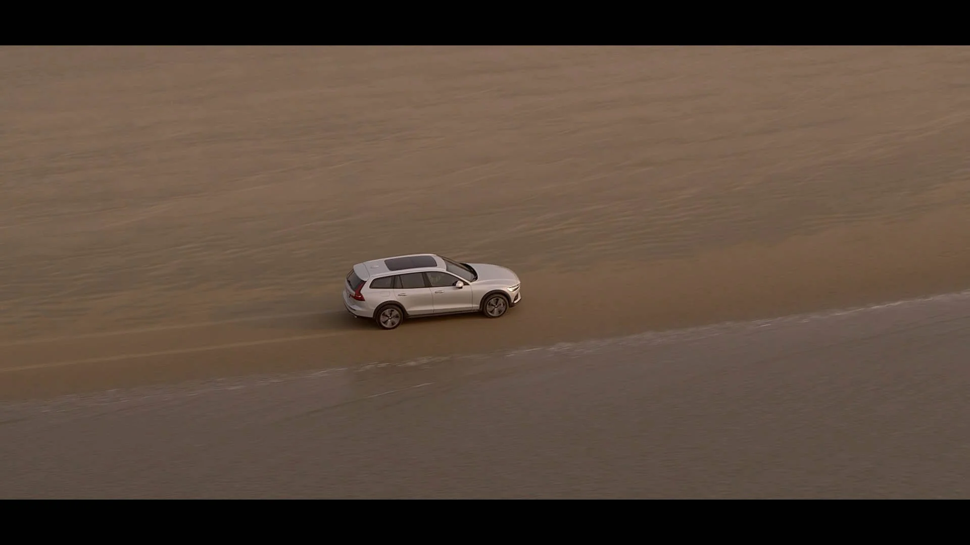 A silver SUV driving on a dirt road through a barren landscape with dry, beige terrain.