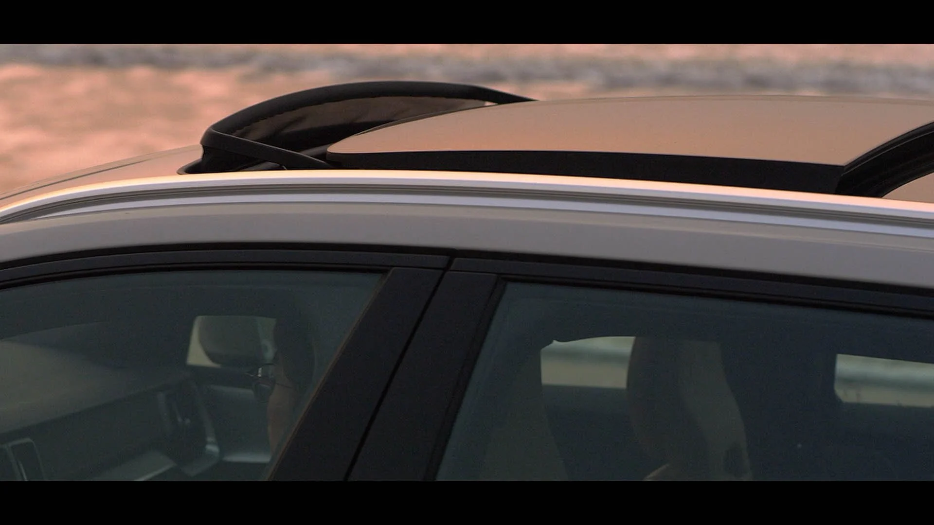 Close-up of a car's roof and sunroof, with a mountain landscape in the background.