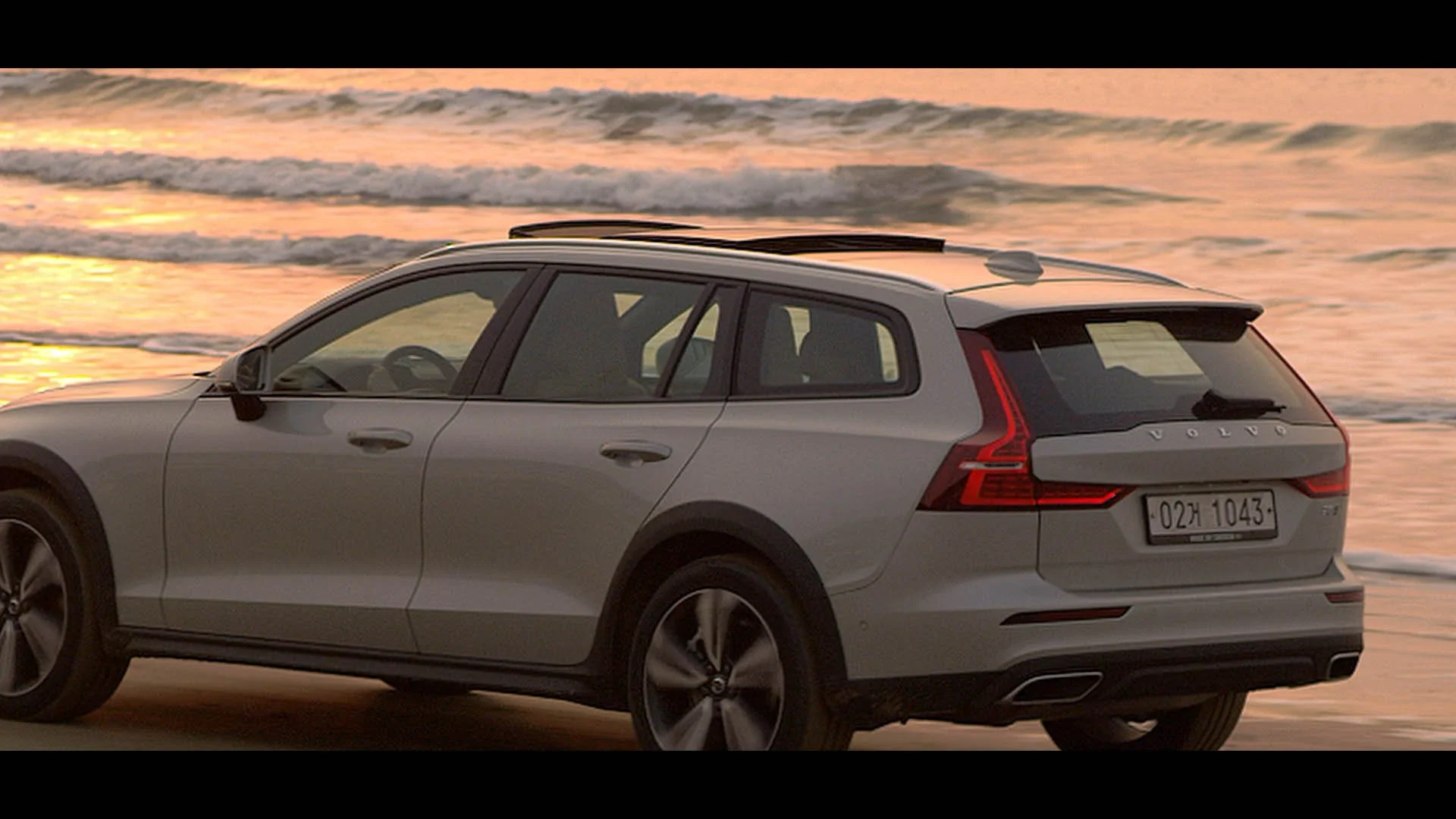 Silver Volvo SUV parked on beach at sunset with ocean waves in background