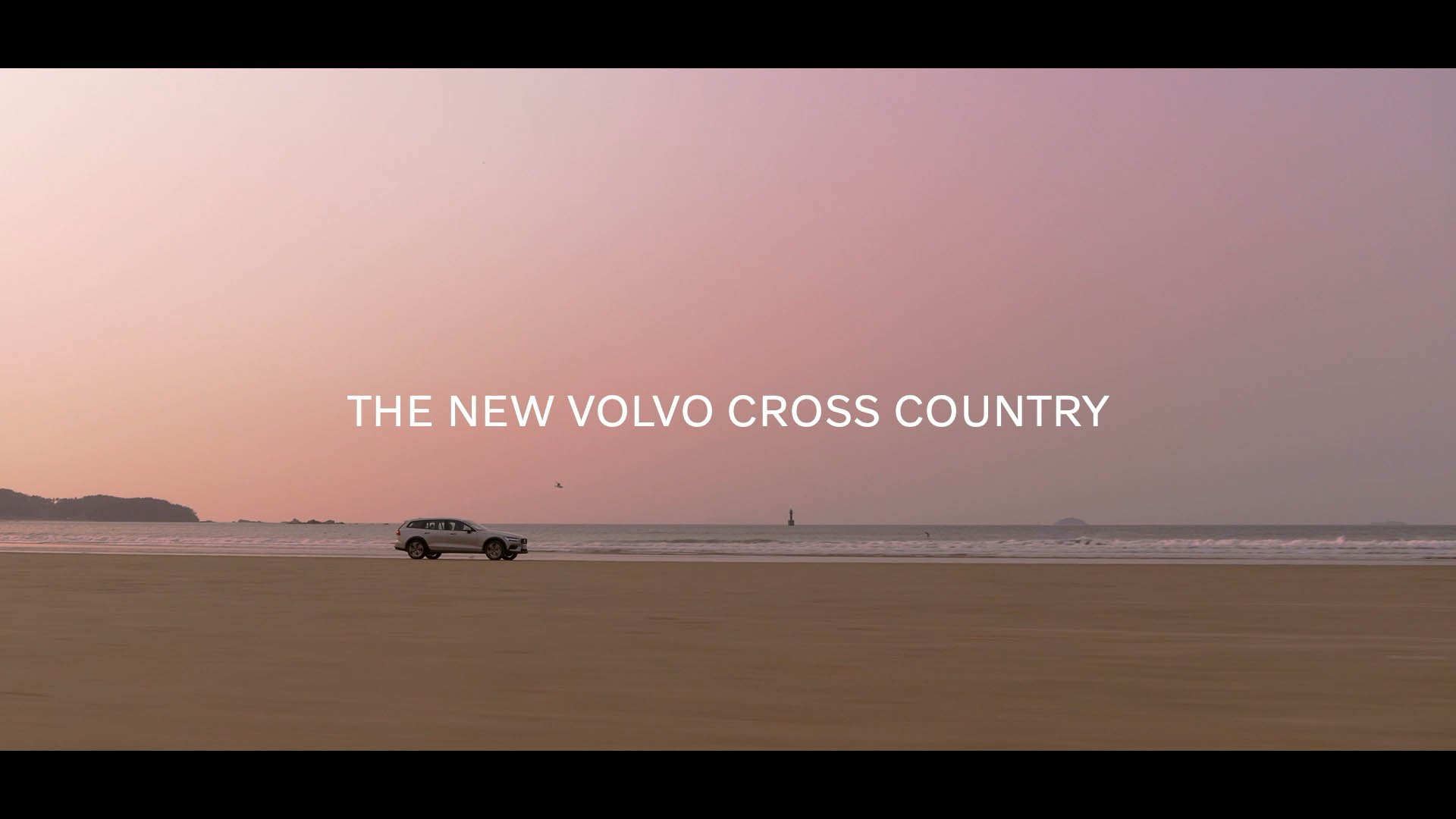 A car parked on a sandy beach at sunset, with a lighthouse in the distance and the text "THE NEW VOLVO CROSS COUNTRY" overlaid on the image.