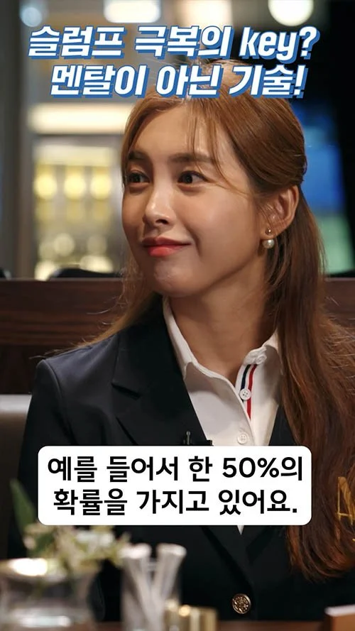 A young woman with light skin and long light brown hair, smiling slightly, sitting indoors. She is wearing a dark blazer and a white shirt with red and blue details. There is Korean text at the top and bottom of the image.