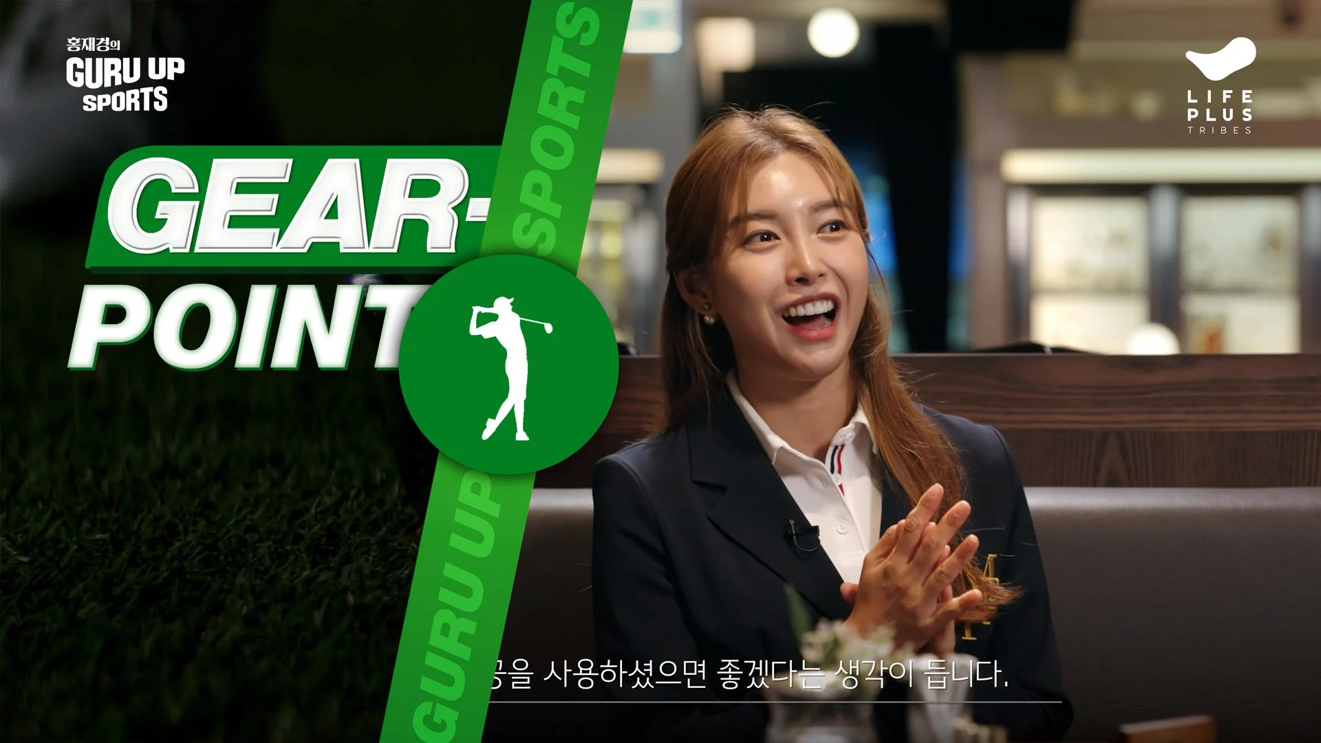 A woman with brown hair in a bun, wearing a dark blazer and white shirt, smiling and talking while seated indoors. There is a green graphic overlay on the left with text "GURU UP SPORTS GEAR POINT" and a white silhouette of a golfer. The background appears to be a kitchen or café with blurred details.