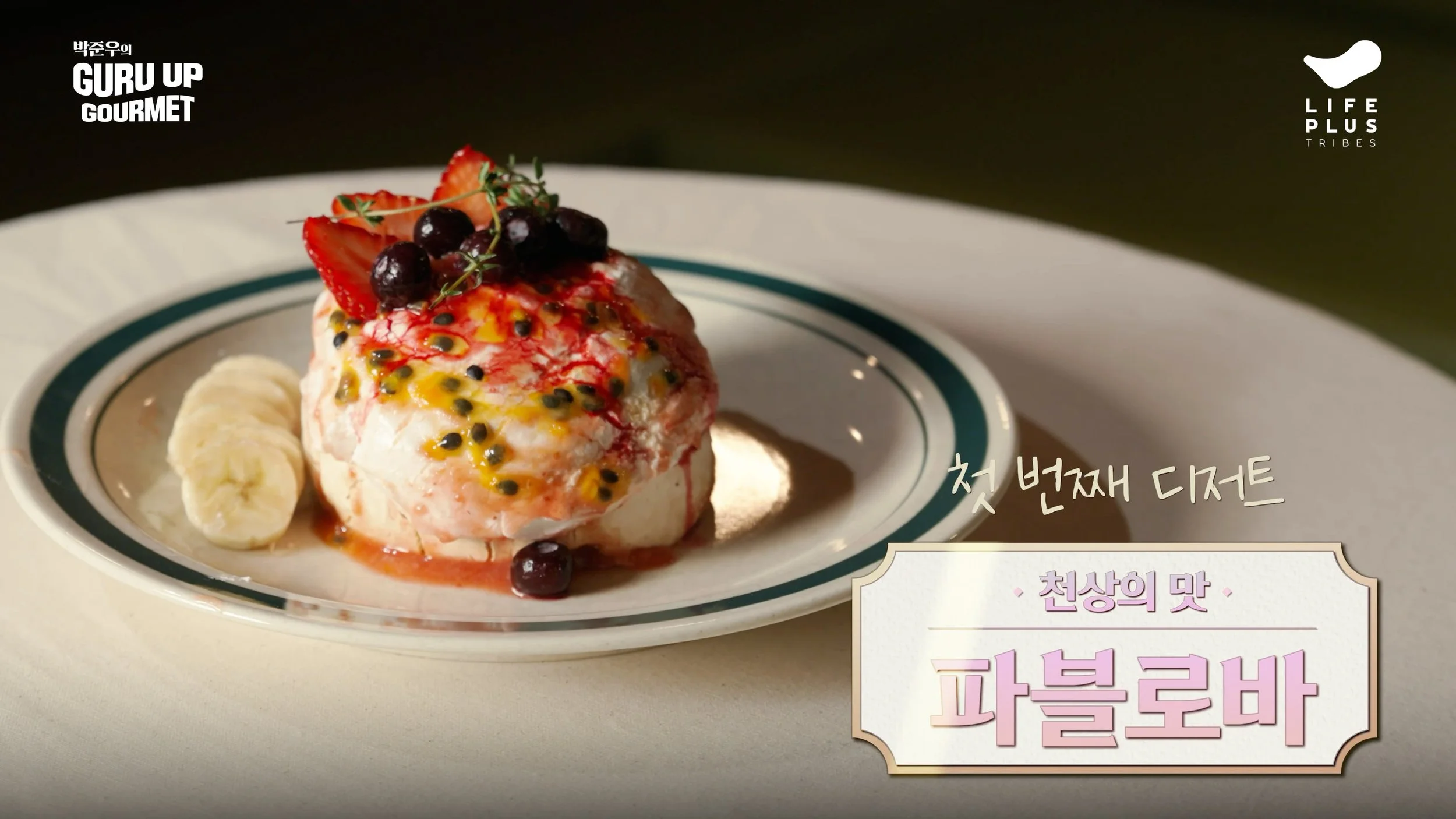 A dessert on a white plate topped with strawberries, blueberries, passion fruit, and a slice of banana, with Korean text and logos in the background.