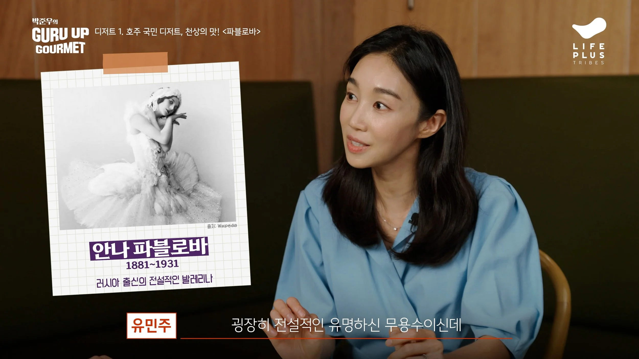A woman with long dark hair, wearing a blue shirt, sitting indoors with a wooden background, appears to be talking. There is a poster in front of her featuring a black-and-white photo of a woman in a ballet costume. The poster contains Korean text, including the name 'Anna Pavlova' with the years 1881-1931, and mentions Russia.