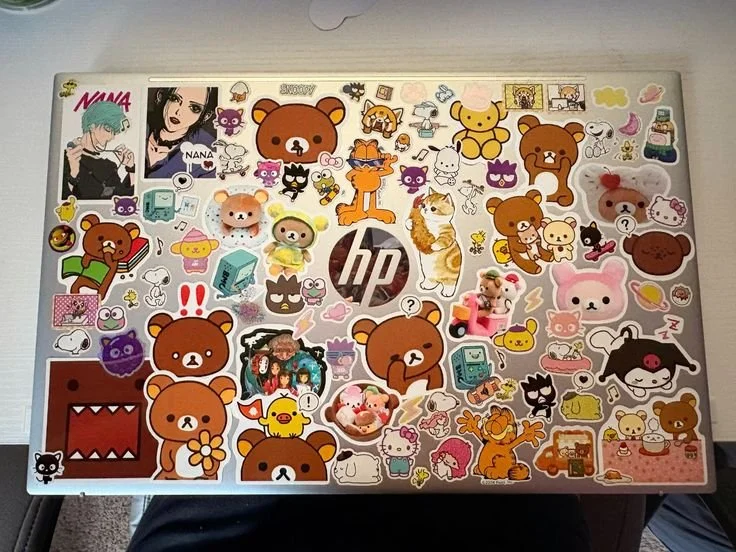 Laptop decorated with numerous stickers featuring Rilakkuma, Korilakkuma, Kiiroitori, and other cartoon characters, animals, and cute designs.