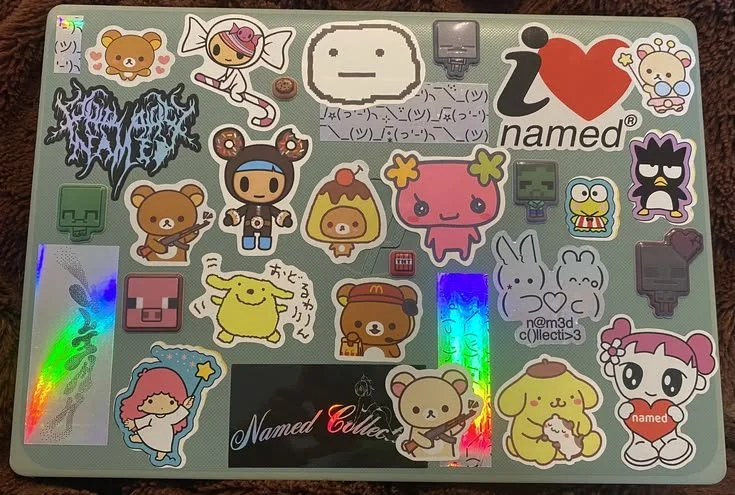A laptop covered with colorful stickers of various cartoon characters, emojis, and gaming icons.