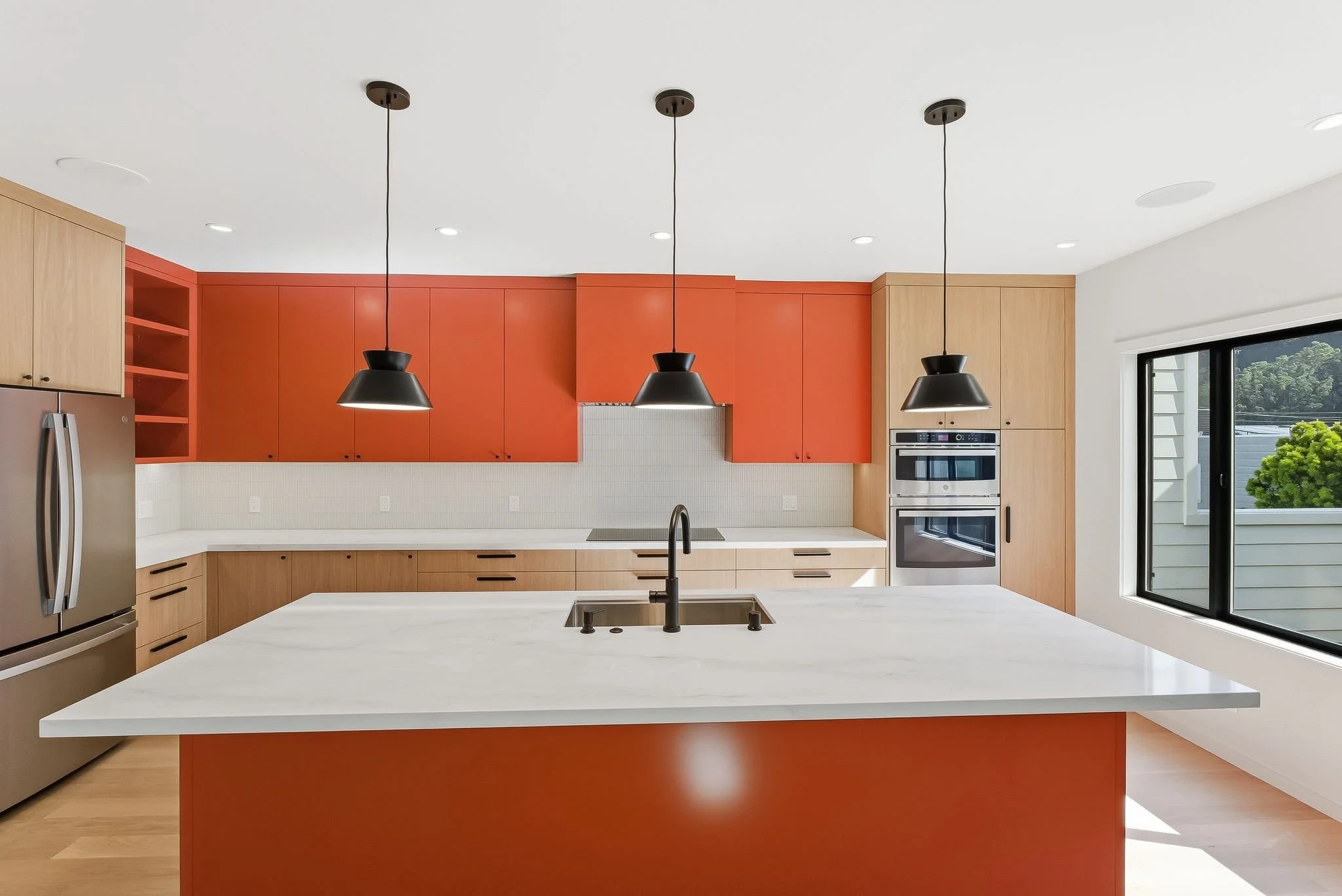 Renovated kitchen with orange upper cabinets, wood lower cabinets, white quartz island, and stainless steel appliances