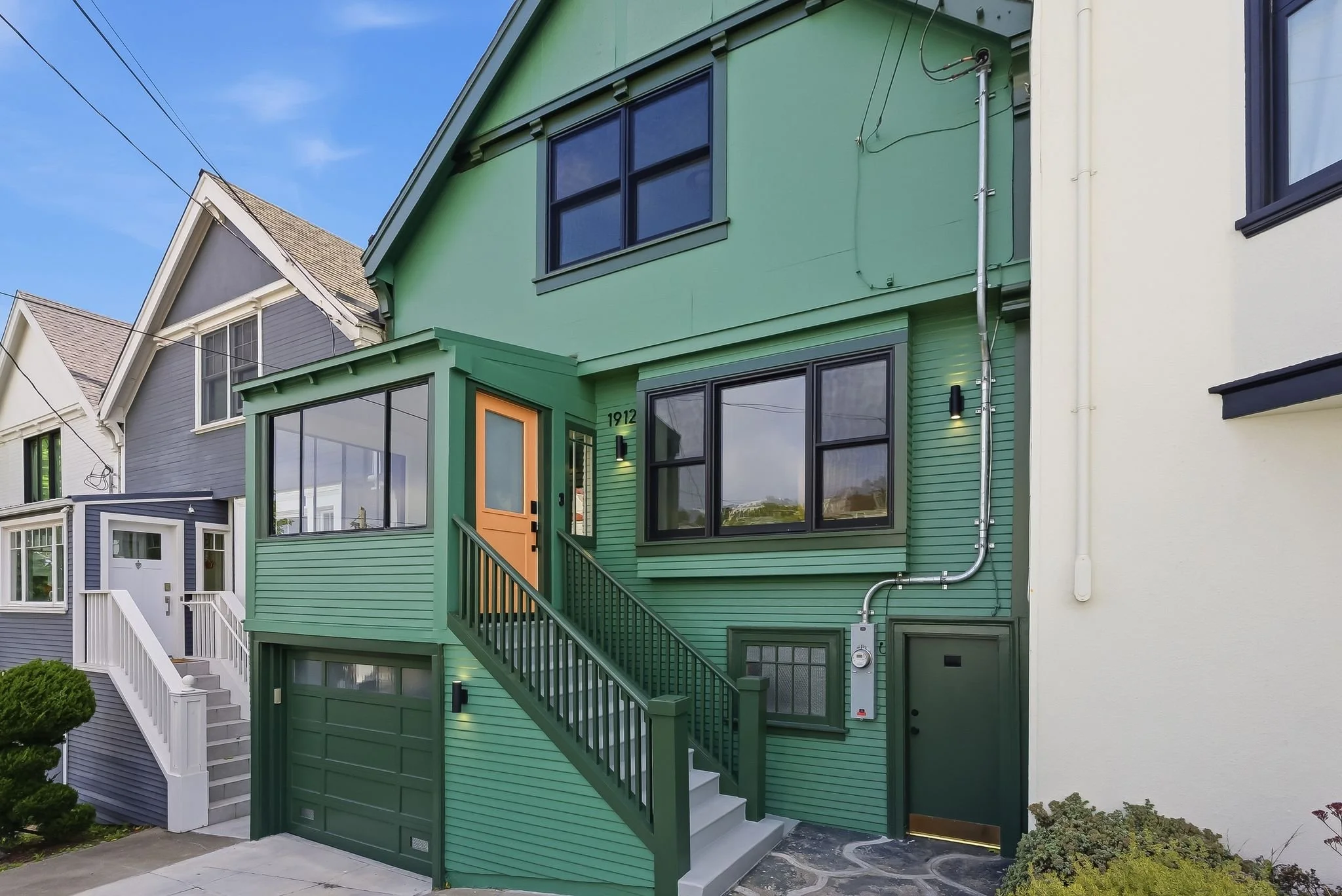 Exterior of a three-story green Victorian-style home with attached garage
