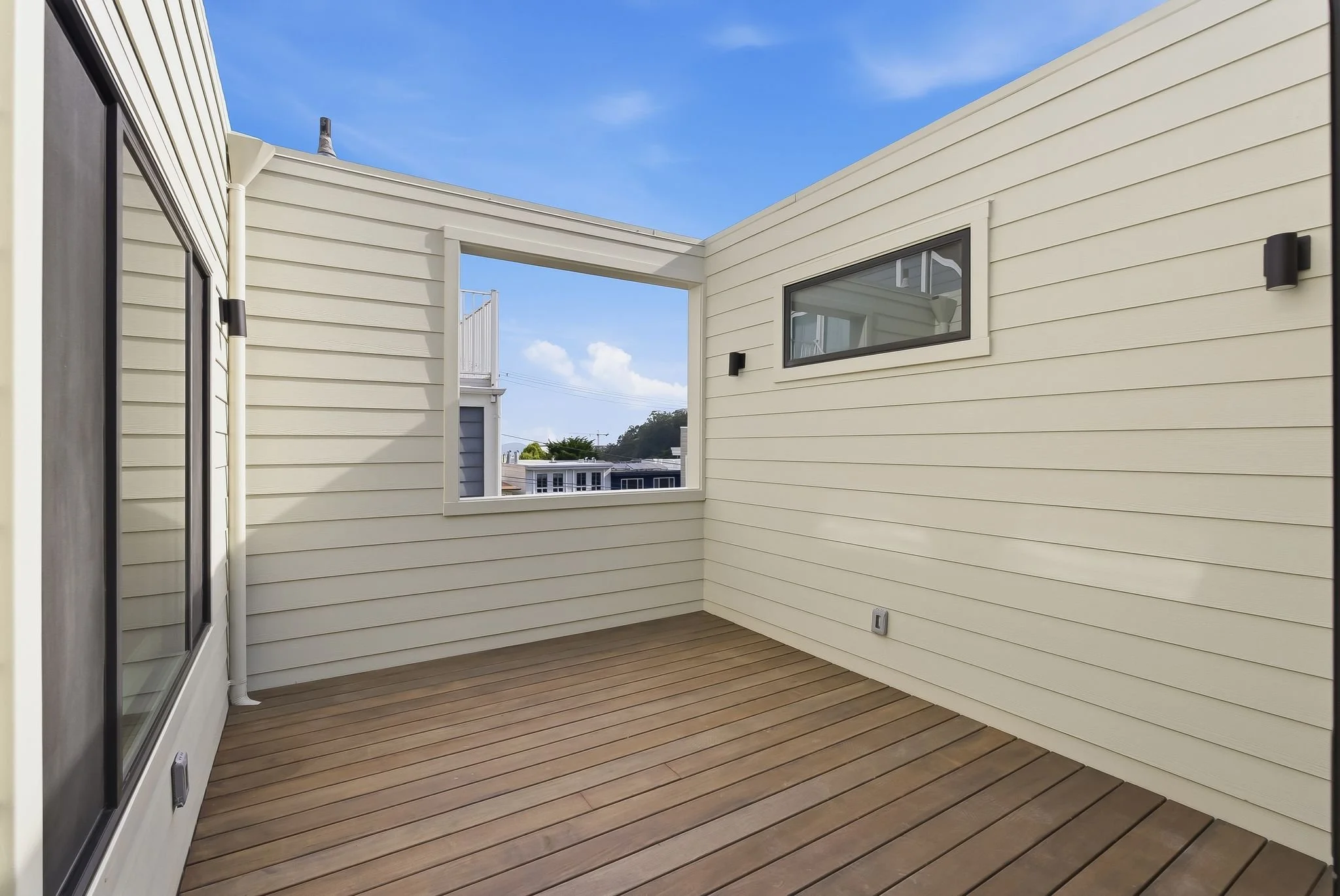 Private wood deck with light horizontal siding and an open-air window framing the sky