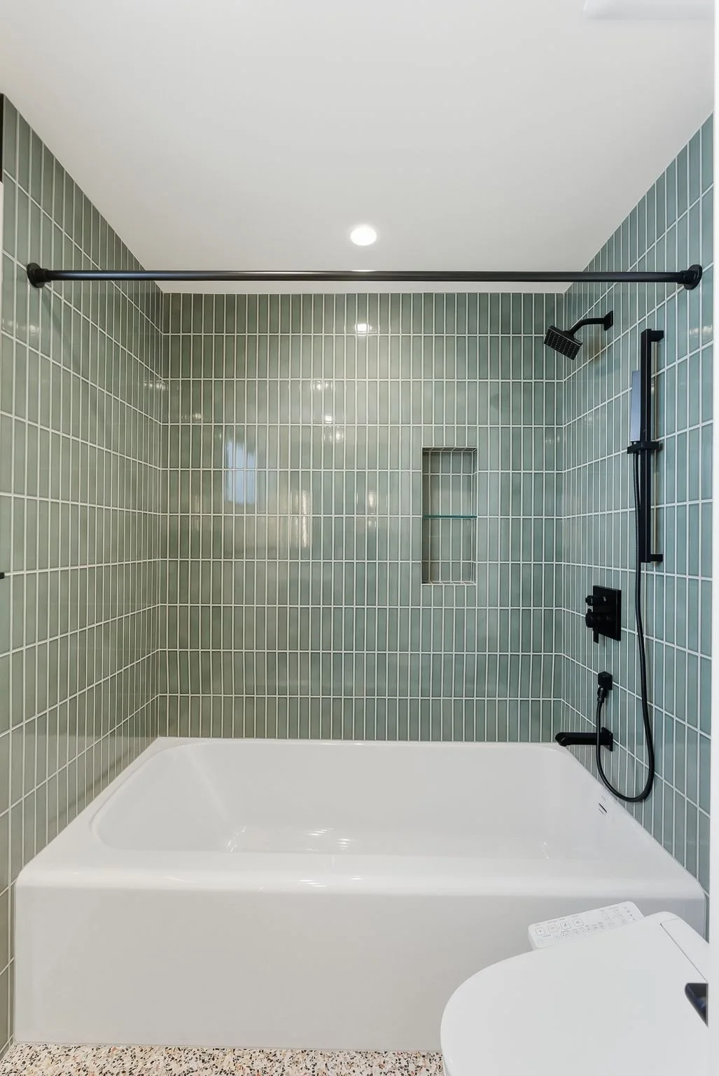 Bathroom with green subway-tile shower surround, white bathtub, and matte black fixtures