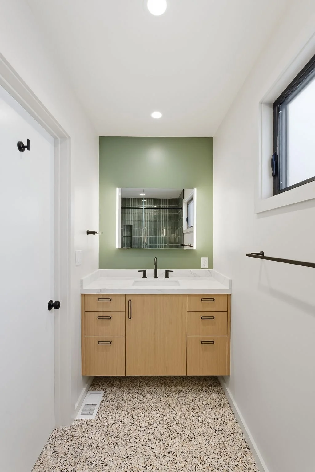 Bathroom vanity with wood cabinetry, white countertop, green accent wall, and terrazzo flooring
