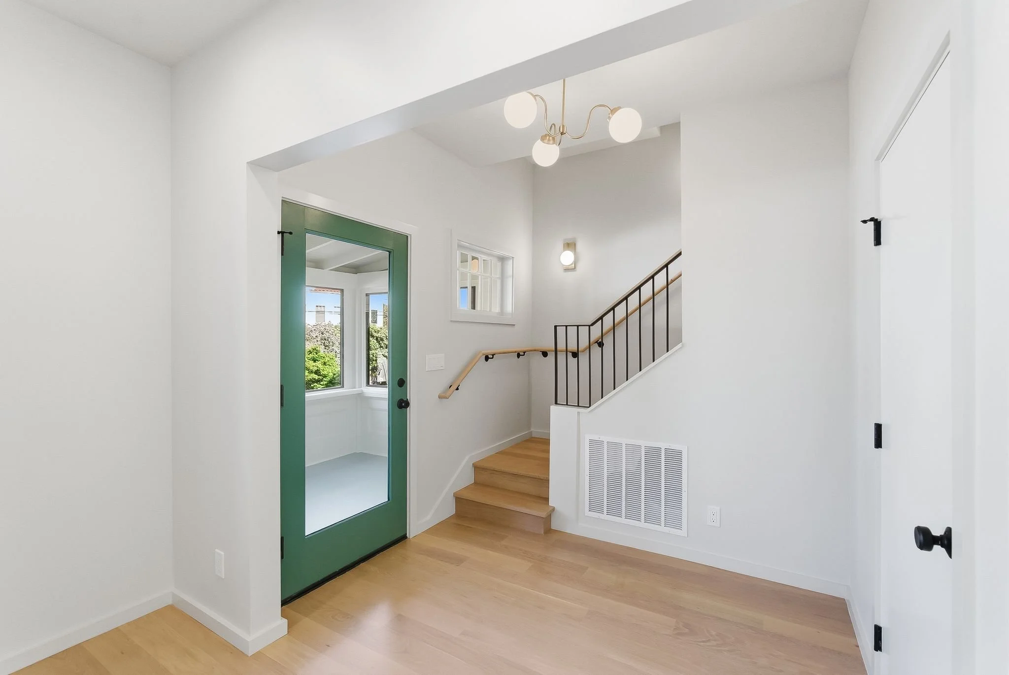 Entry hall with a green front door, staircase, and light hardwood floors