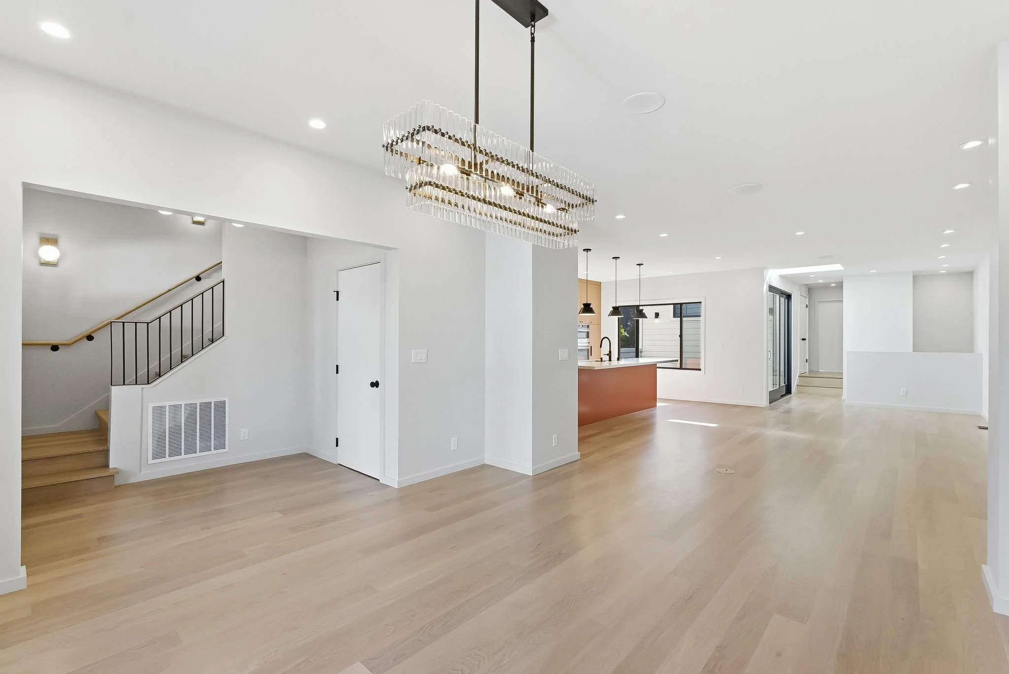 Open-plan living and dining space with wood floors, a linear pendant light, and staircase
