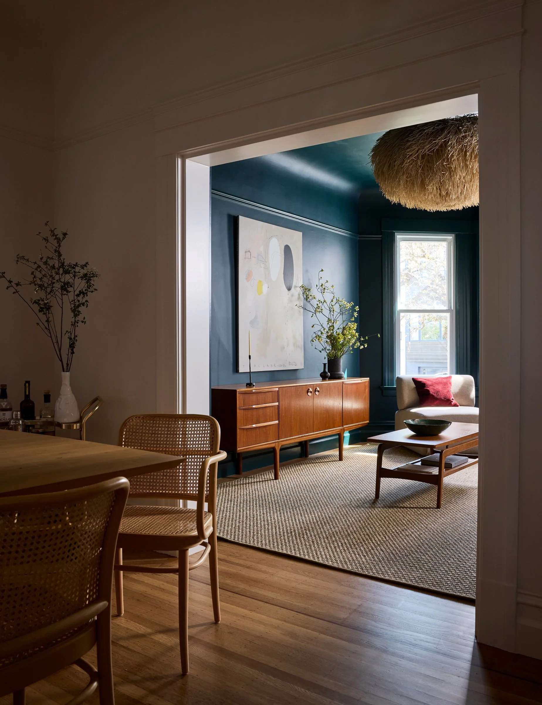 Open-plan view from the wood-and-cane dining area through a doorway into the navy living room