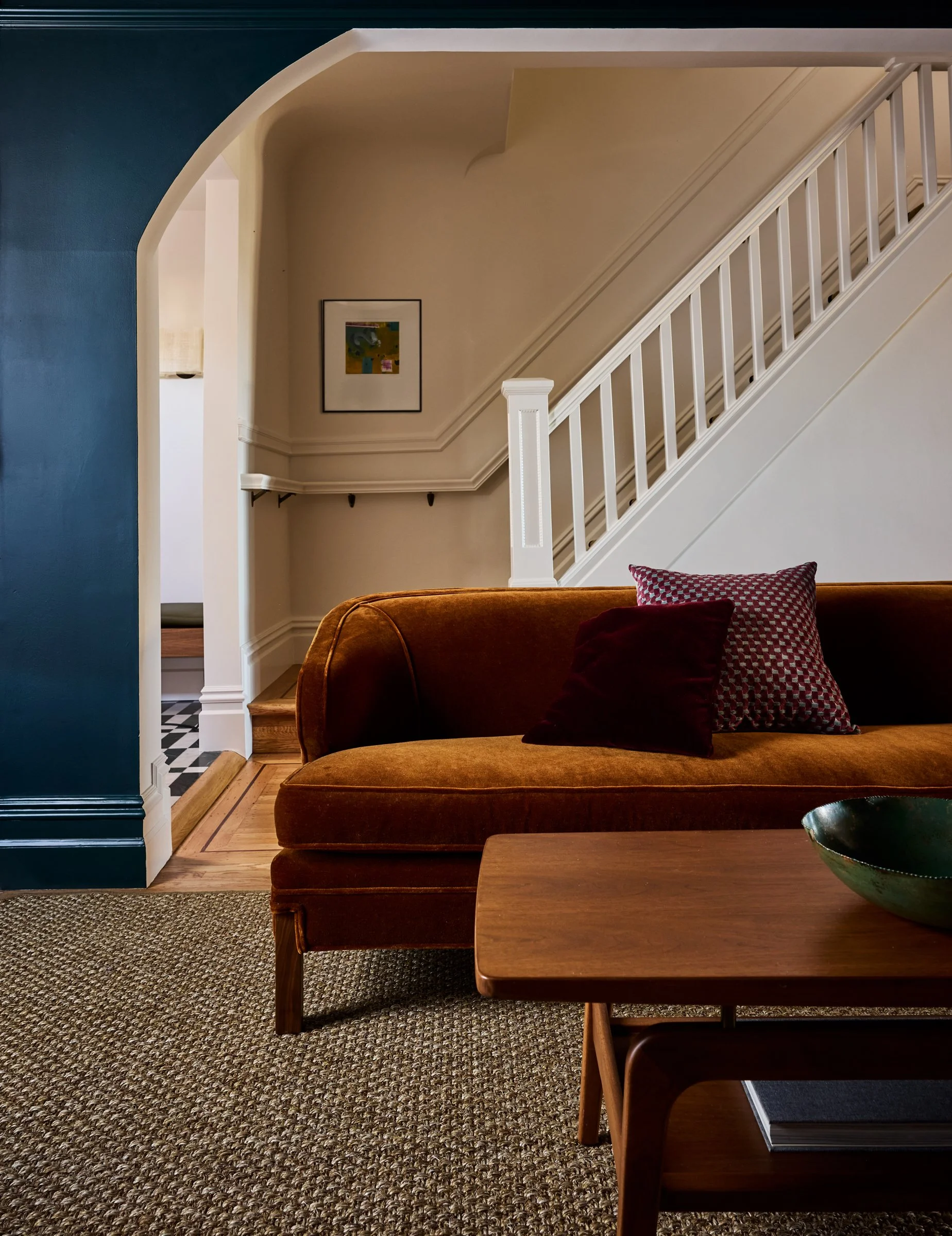 Living room with navy walls, a cognac velvet sofa, wood coffee table, and a white staircase with banister